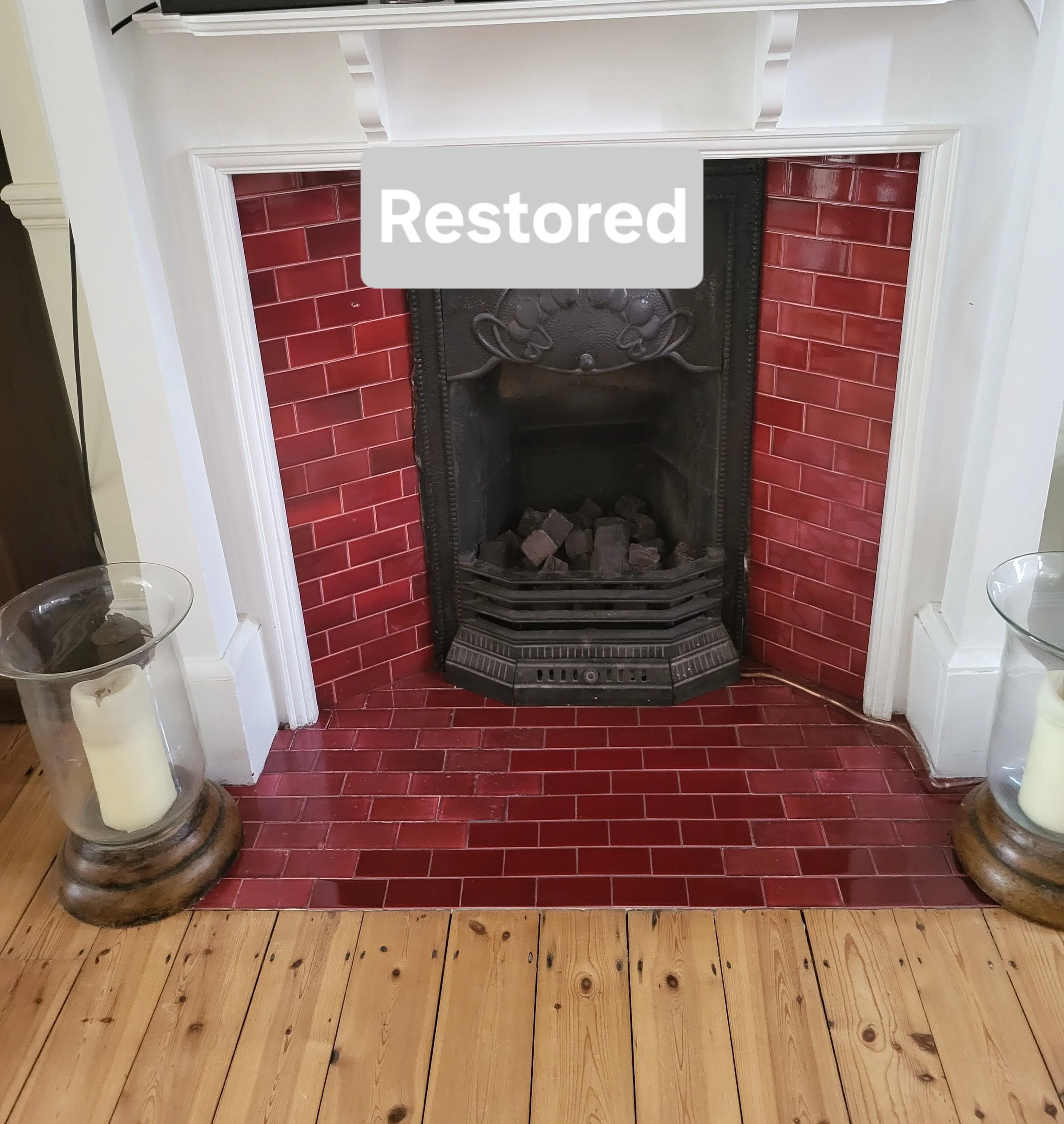 Restore fireplace with red bricks, black cast iron grate, white mantel and two glass candle holders with candles on either side.