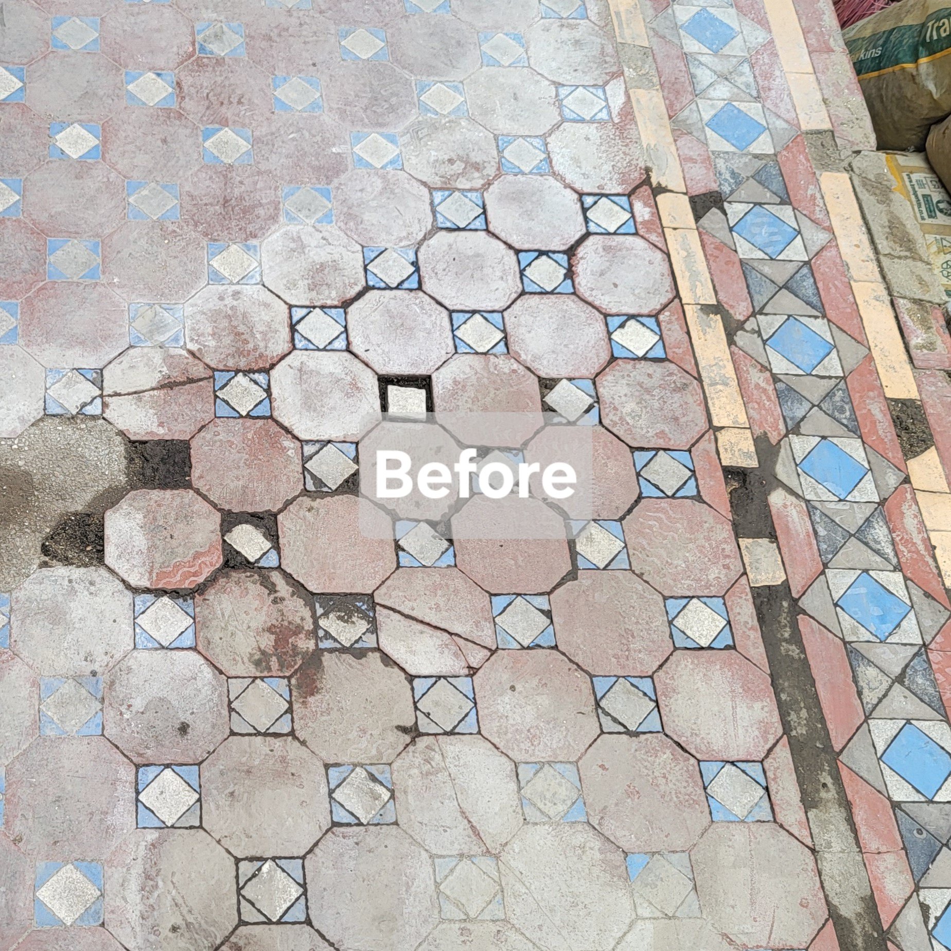 Old and damaged hexagonal and square patterned tile flooring with some broken tiles and grout cracks, alongside a partially visible bag of construction material.