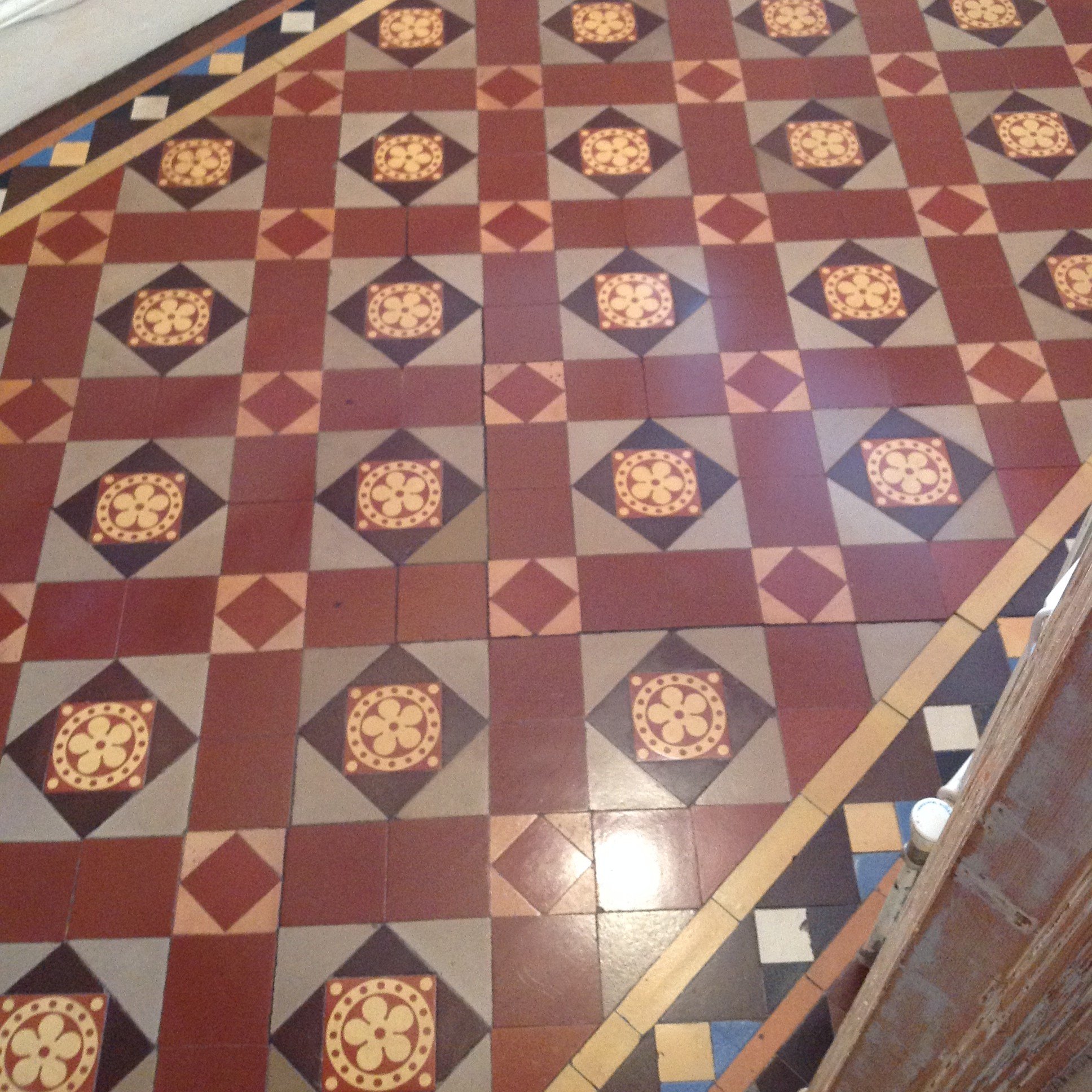 A patterned tiled floor with geometric designs in red, black, beige, and cream. The pattern repeats in a geometric fashion with a border on one side.