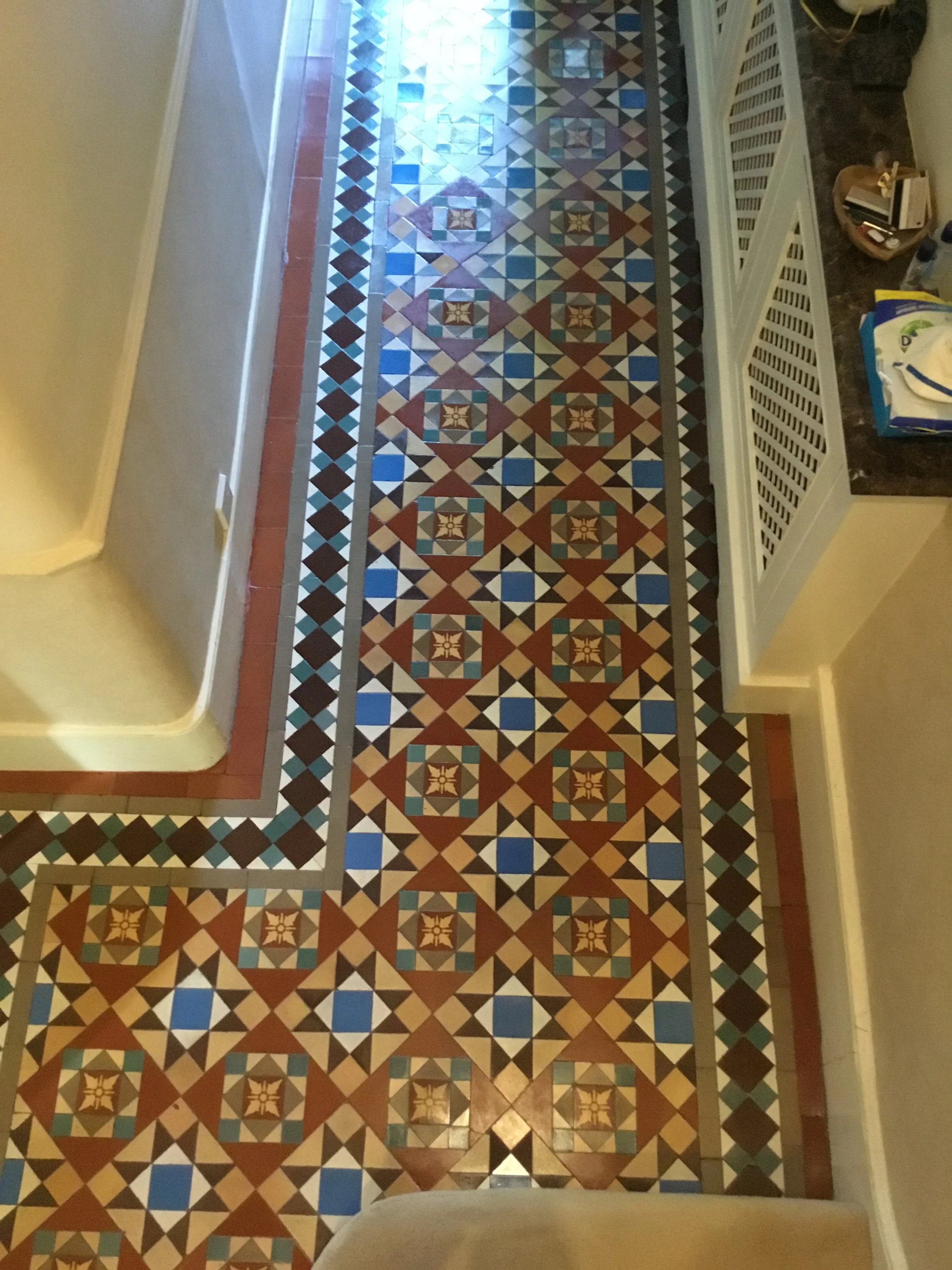 Patterned mosaic tile floor in a hallway with geometric designs and various colors including blue, brown, beige, and white.