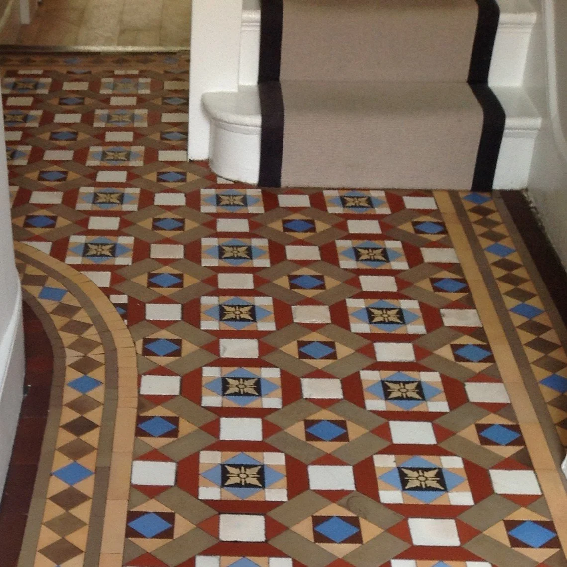 Close-up of patterned ceramic tile floor leading to the stairs decorated with a beige carpet runner bordered with black