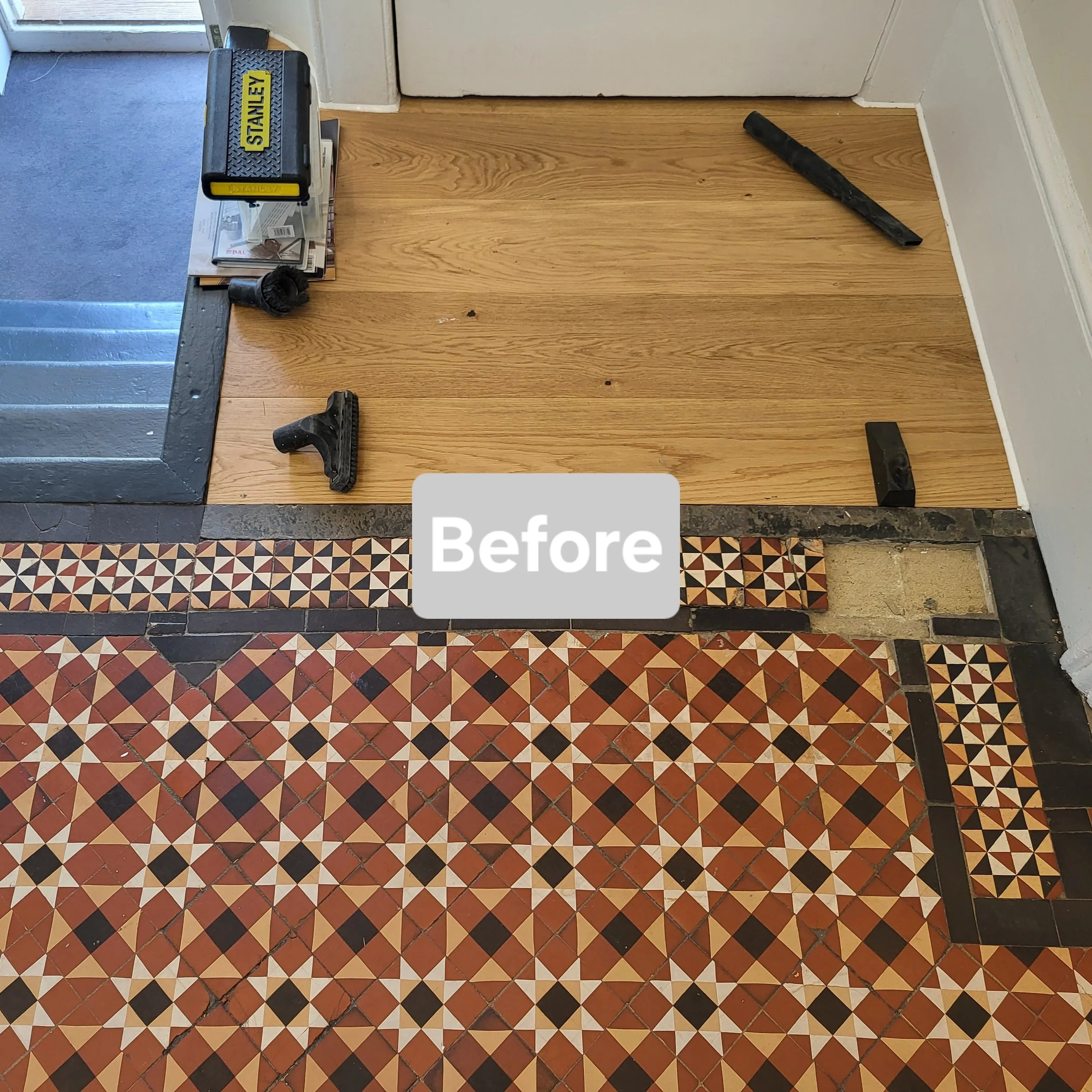 A floor with patterned tiles and an area with wood flooring, showing tools and supplies used for replacing or repairing the flooring.