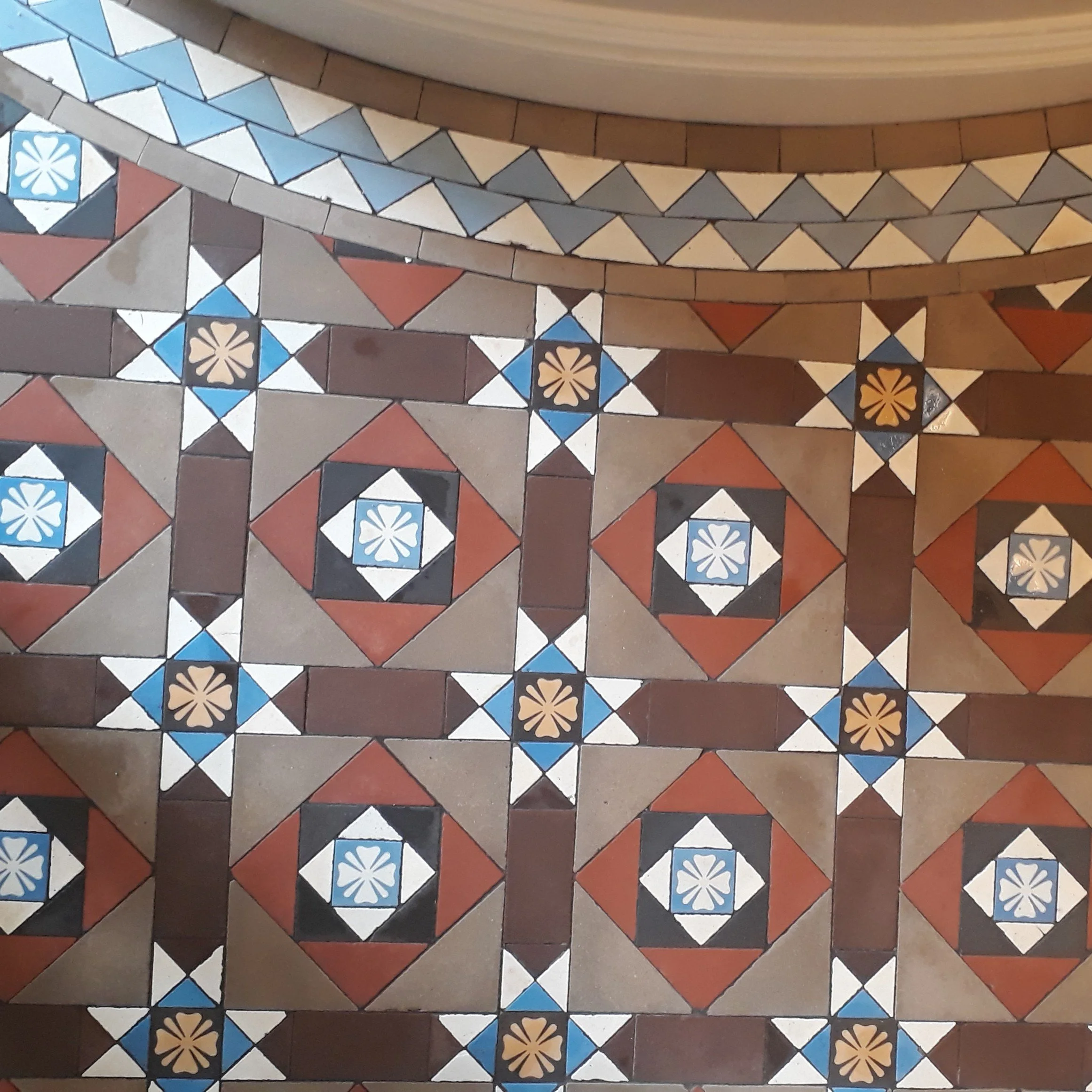 Colorful patterned floor tiles with geometric designs in red, black, white, blue, beige, and brown.