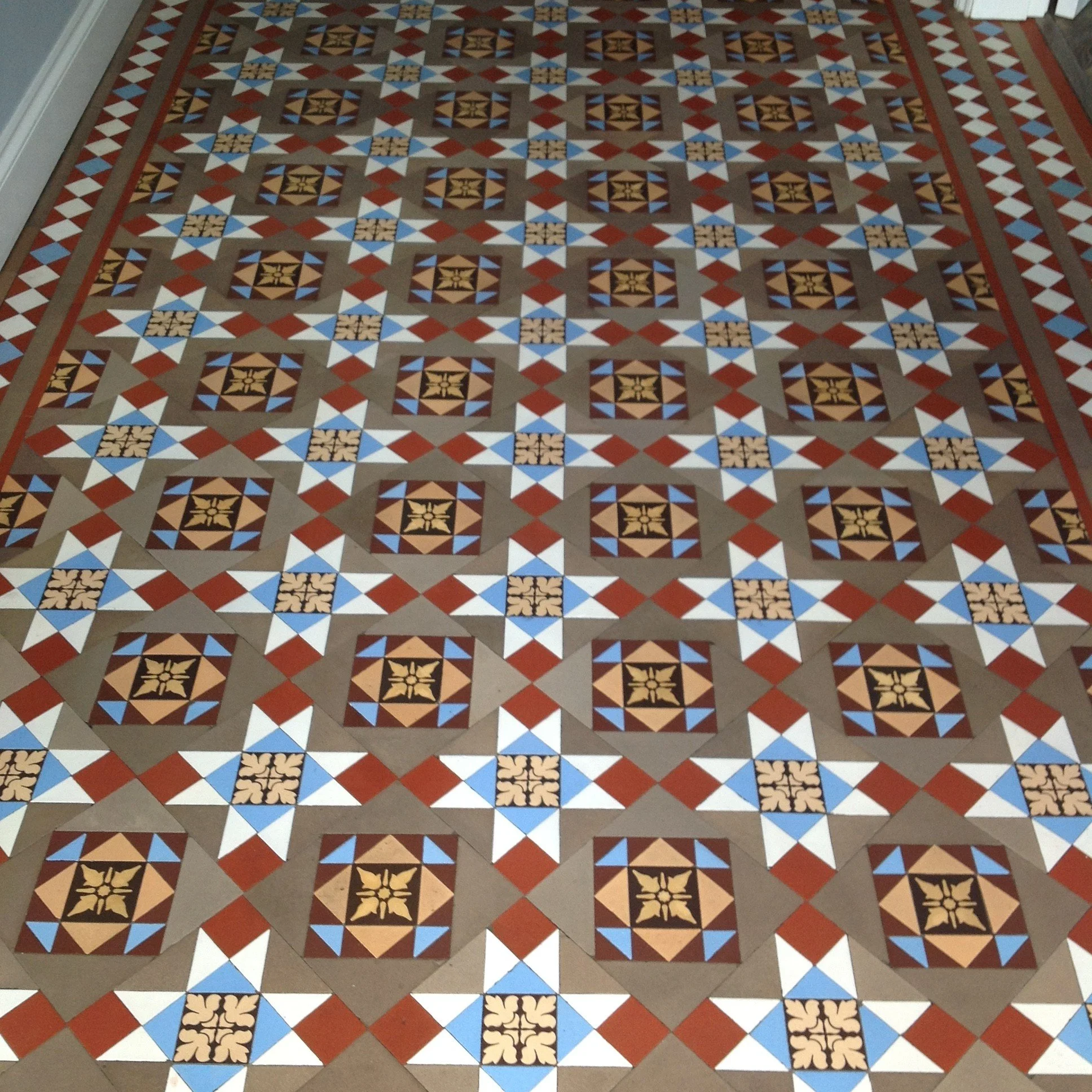 Decorative tiled floor with geometric patterns including squares, triangles, and star shapes in brown, blue, white, and black colors.