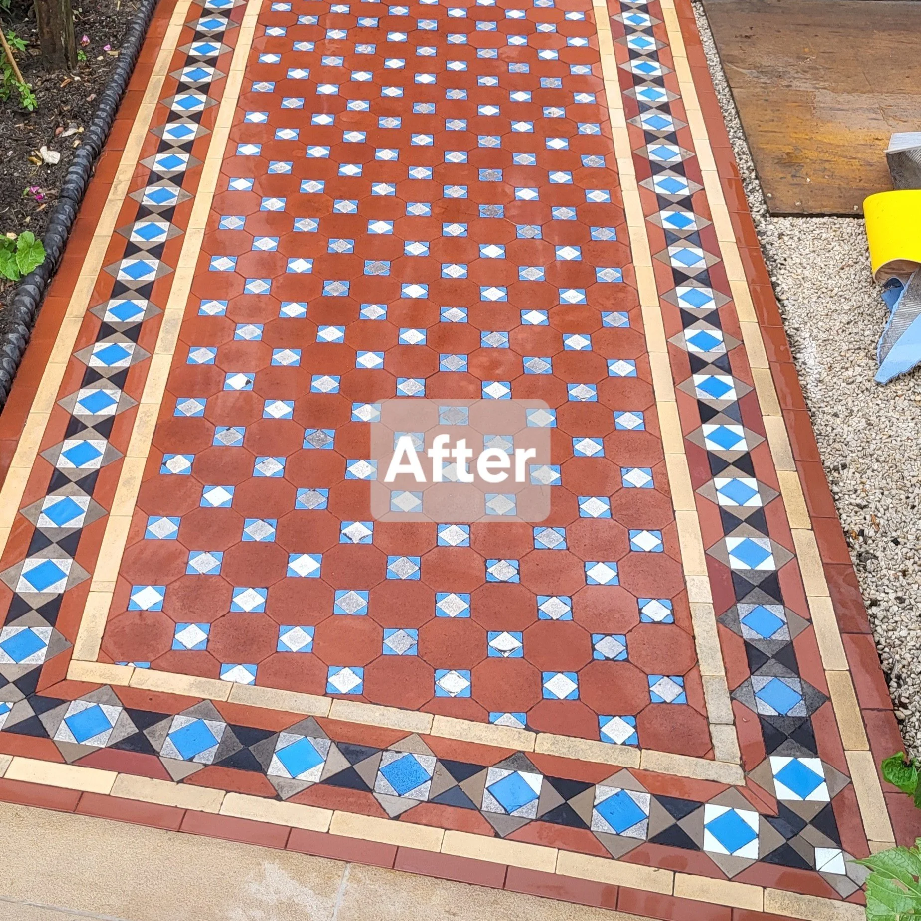 Colorful tiled walkway with geometric patterns, framed by borders, with soil and plants on the side and gravel on the right.