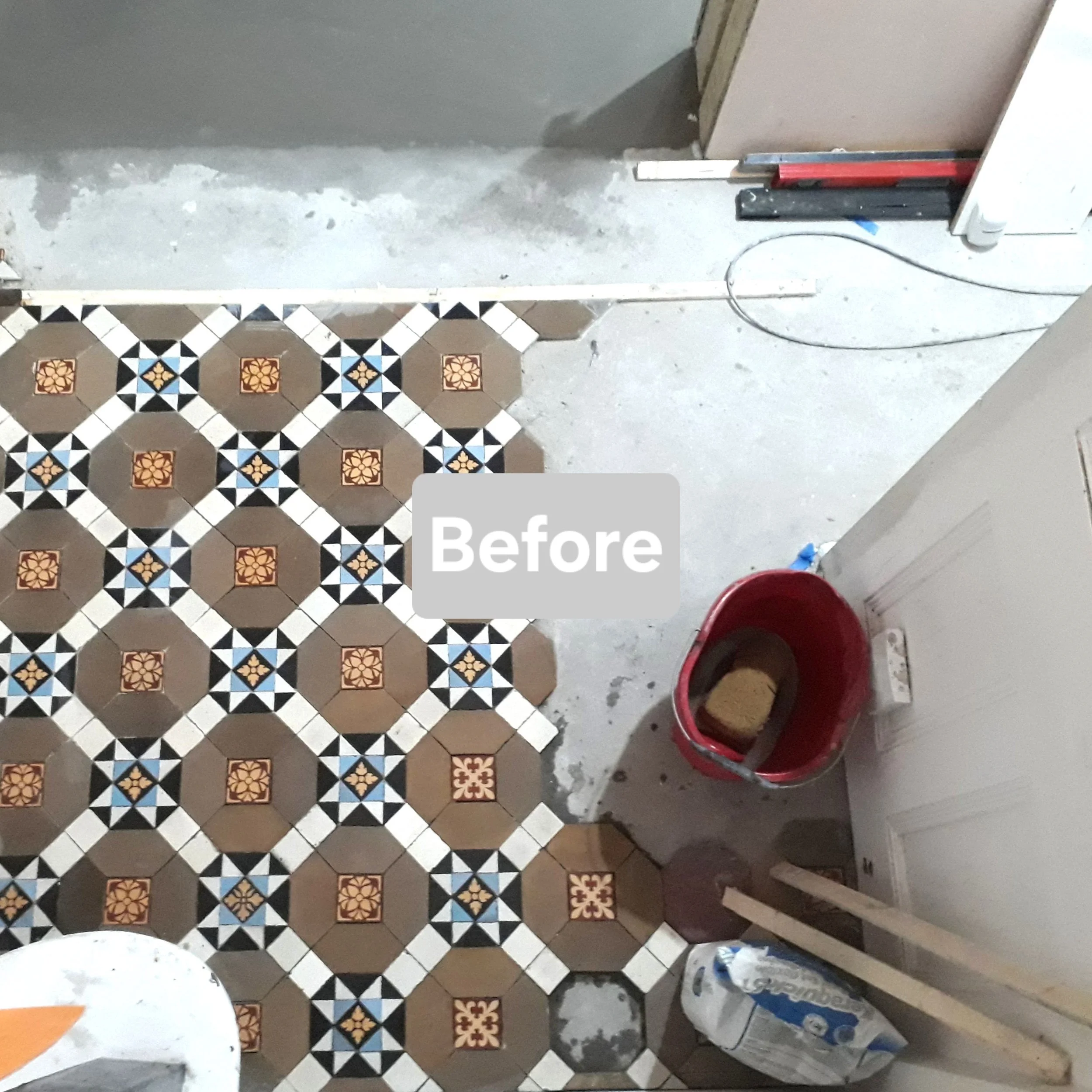 Floor with geometric patterned tiles, partially removed, in a room under renovation. There are construction tools, a bucket of grout, and construction materials visible.