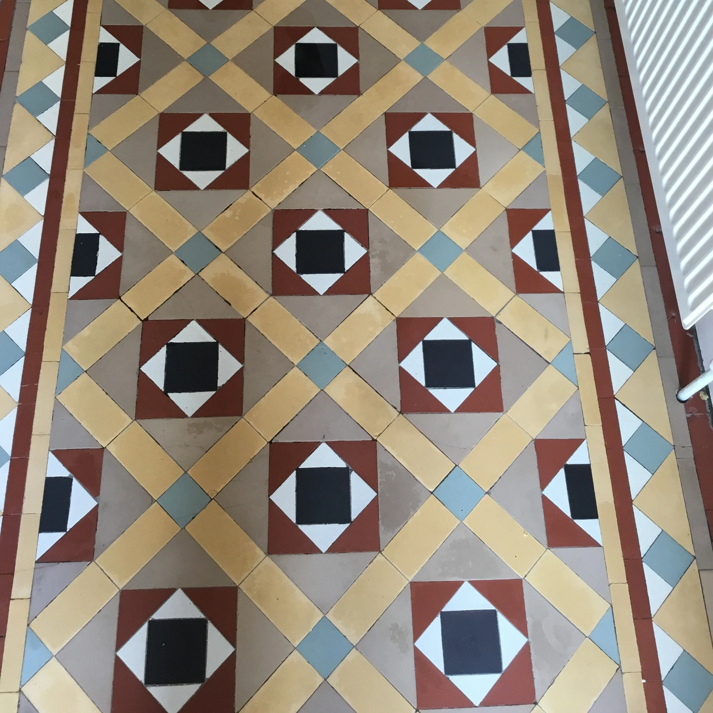 Patterned tile floor with geometric shapes in red, black, white, blue, and beige, bordered by a white radiator on the right side.