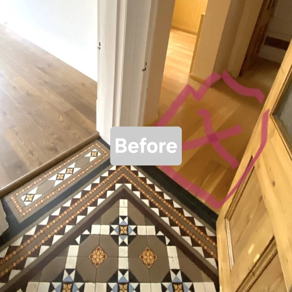 Hallway with patterned tile flooring in shades of black, white, beige, and blue, leading to a wooden room. A pink outline of a pair of shoes is drawn on the wooden floor near the entrance.