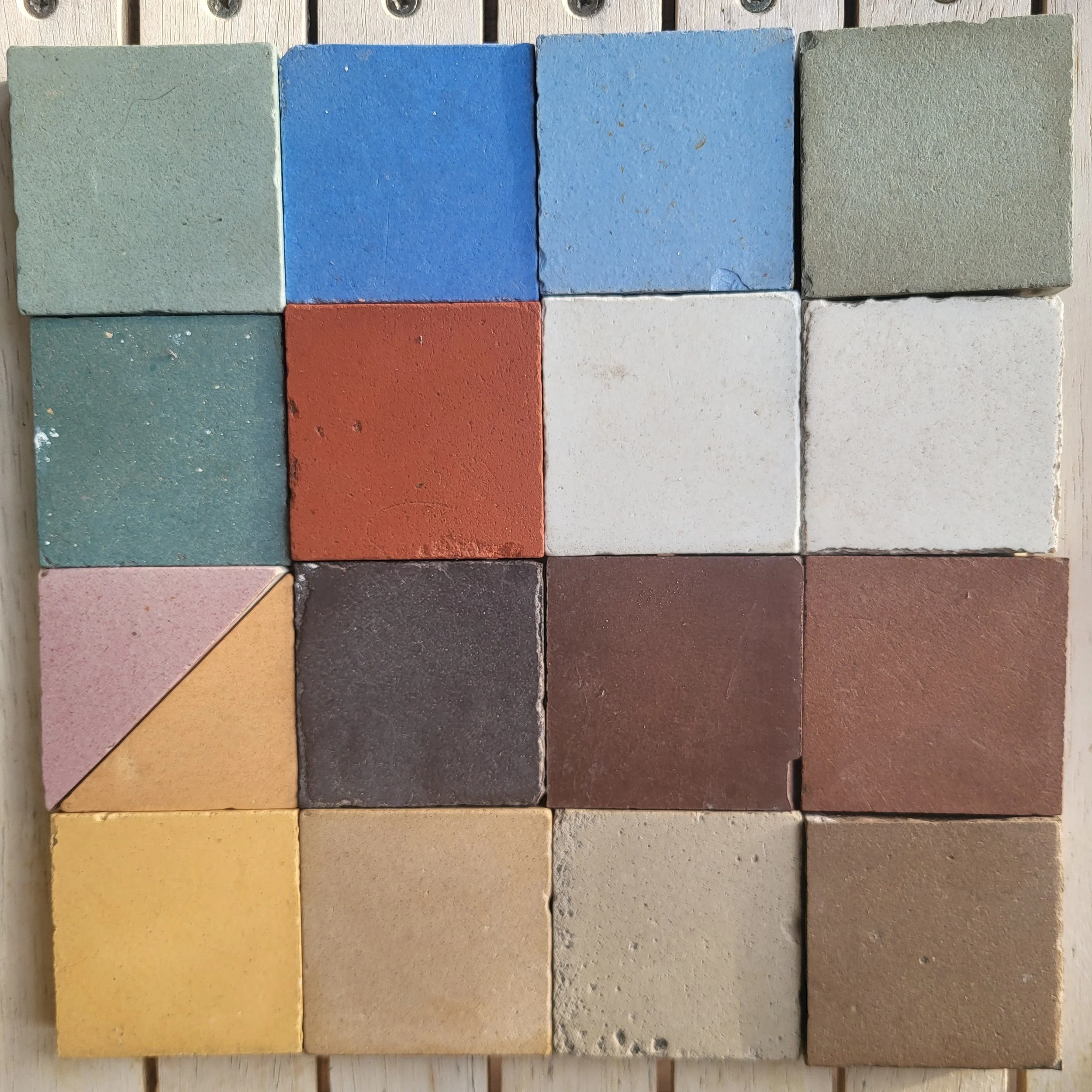 A collection of 12 concrete bricks arranged in four rows and three columns, with various colors including green, blue, red, yellow, black, and gray, on a wooden surface.