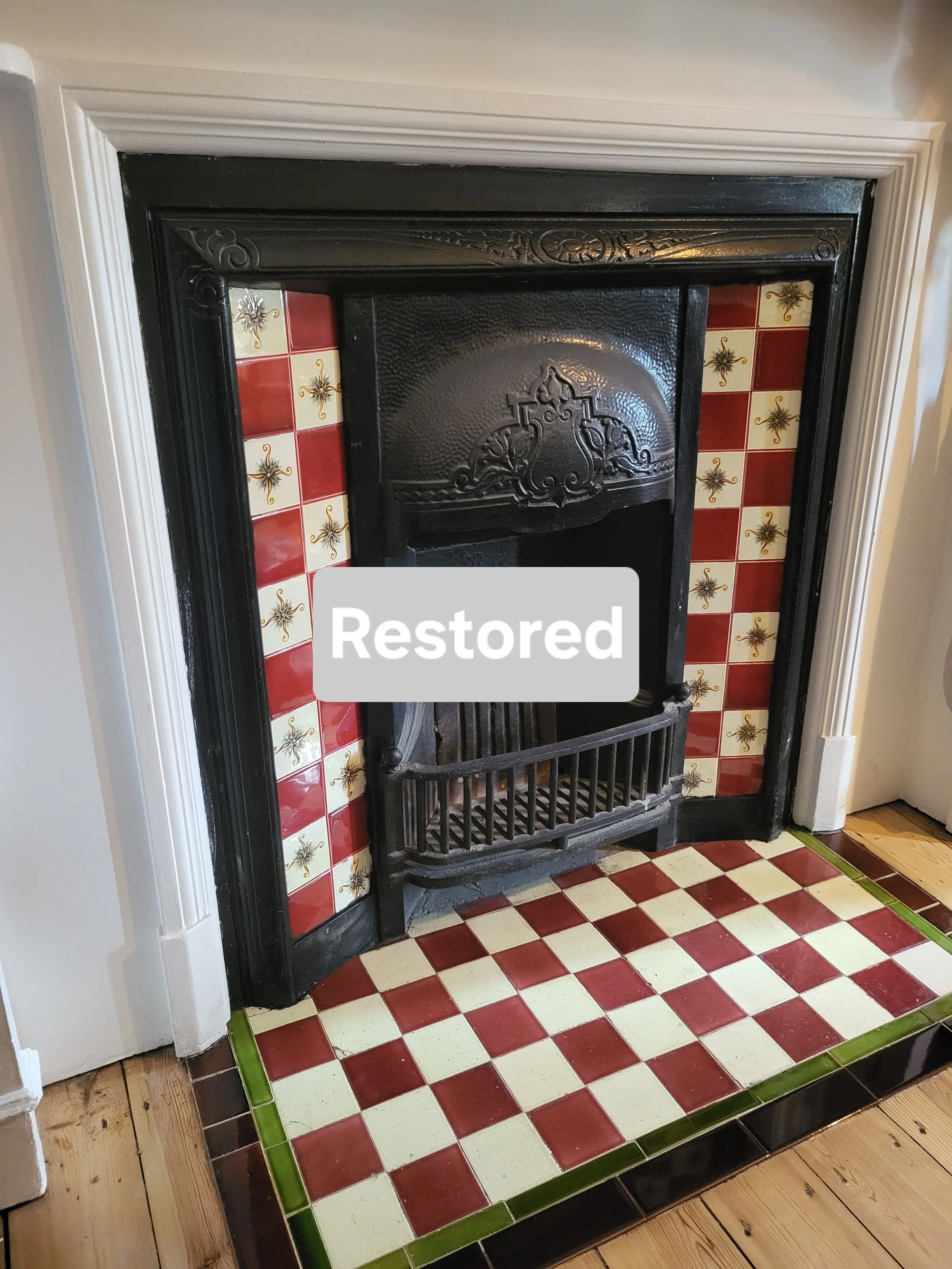 Restored vintage fireplace with decorative black cast iron surround and red and cream checkered tile hearth.