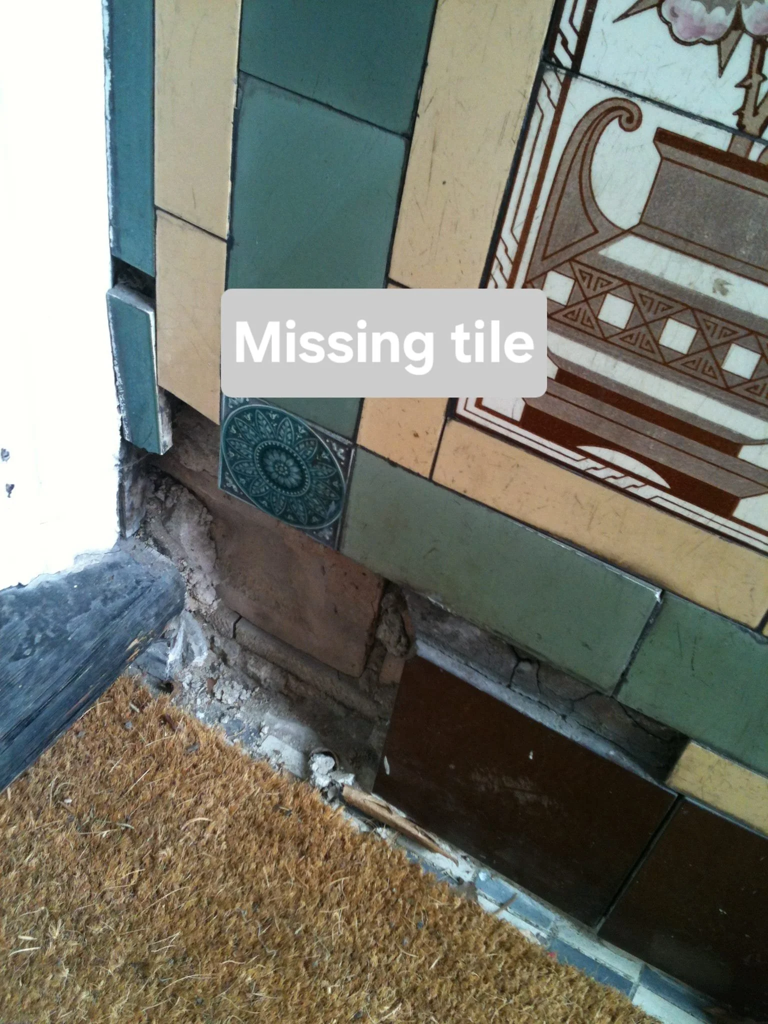 Image shows partially tiled floor near a doorway, with a missing tile and visible gap revealing underlying bricks and concrete. Carpeting is seen at the bottom.