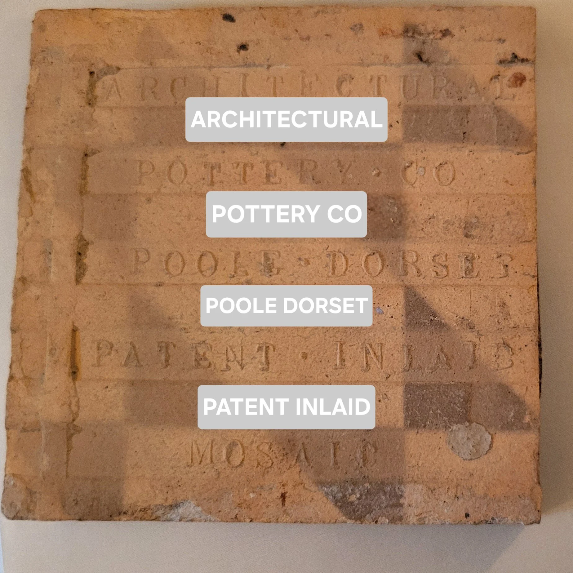 A brick showcasing engraved text including the words 'ARCHITECTURAL', 'POTTERY CO', 'POOLE DORSET', 'PATENT INLAID', and 'MOSAIC'.