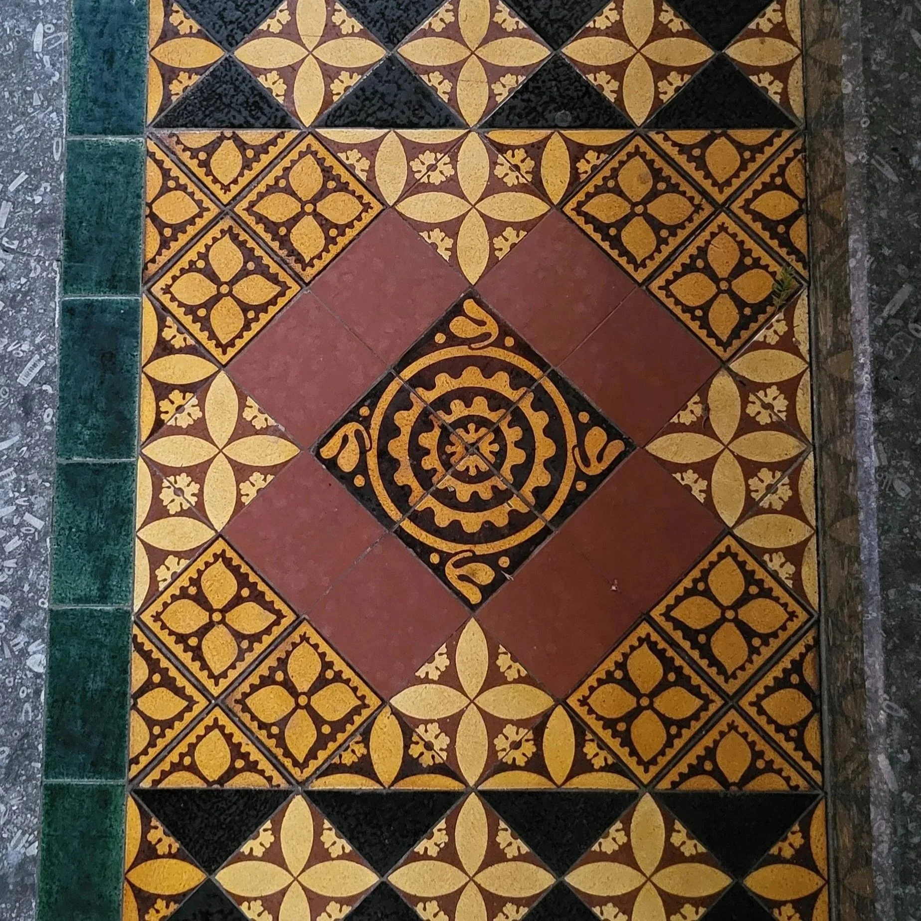 Decorative encaustic tiles with intricate floral and geometric patterns bordered with a glazed green tile, laid in a Surrey church