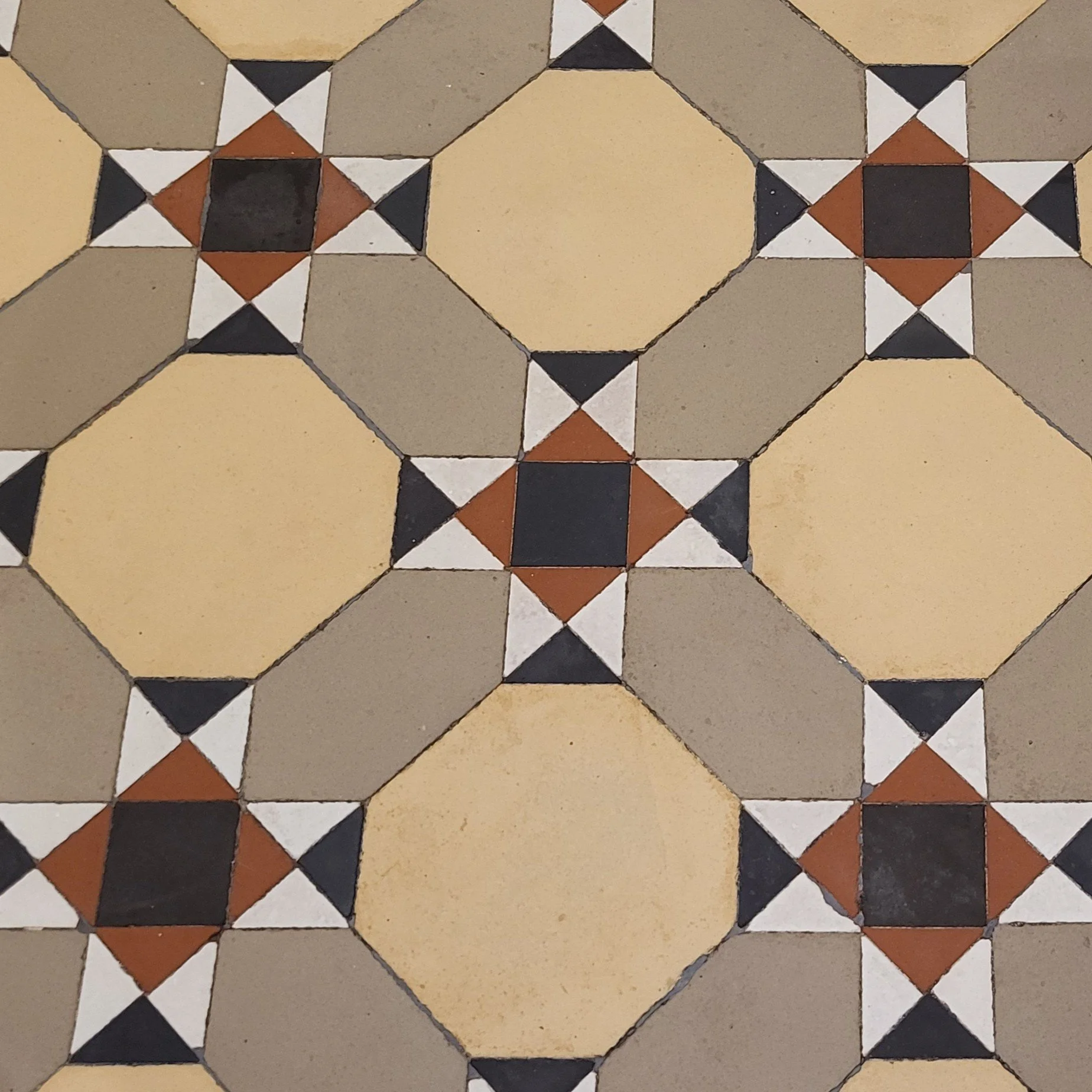 Pattern of decorative floor tiles with beige squares, black and white triangles, and brown accents forming geometric designs.