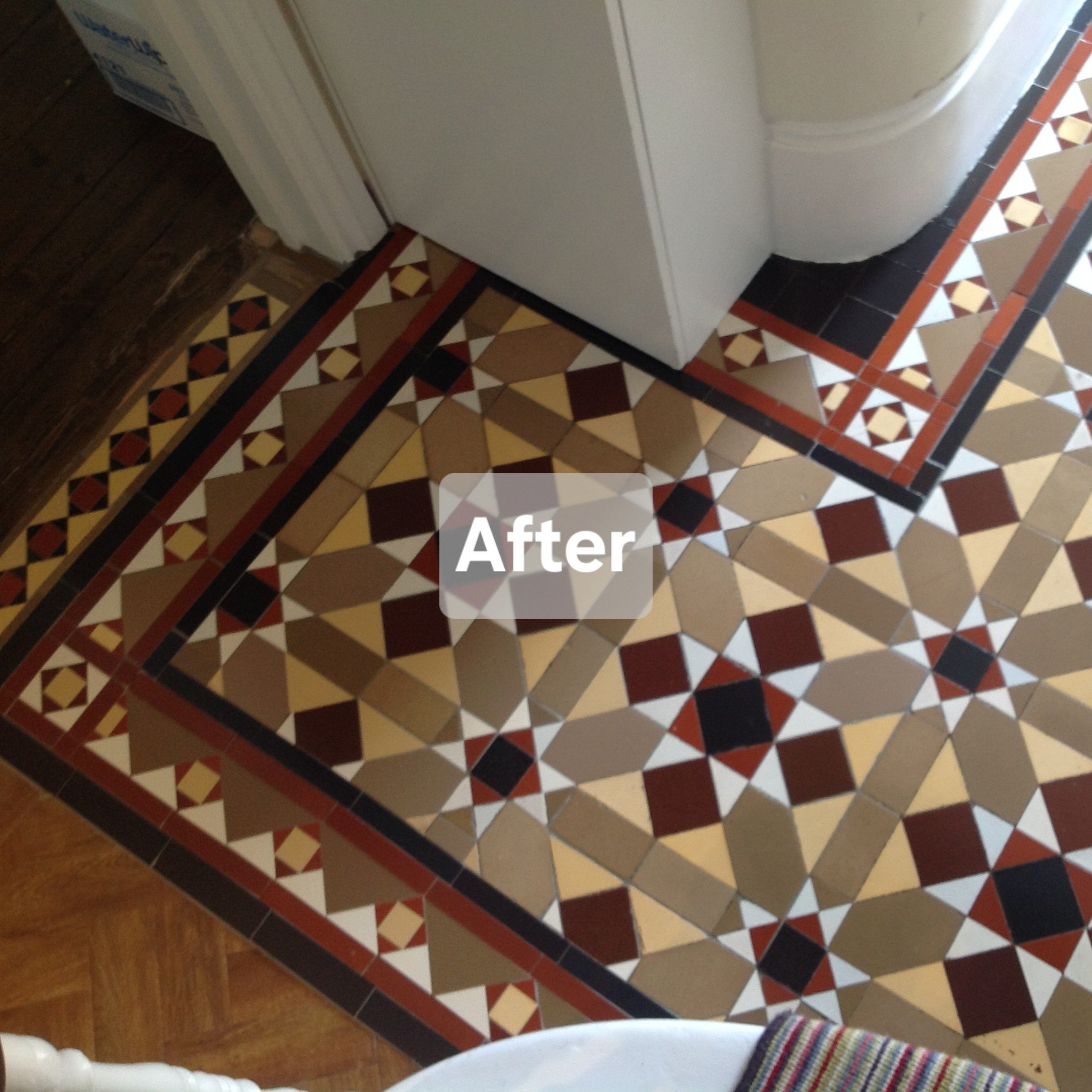 The end of a period tiled hallway near the stairs and adjoining a wooden floor.