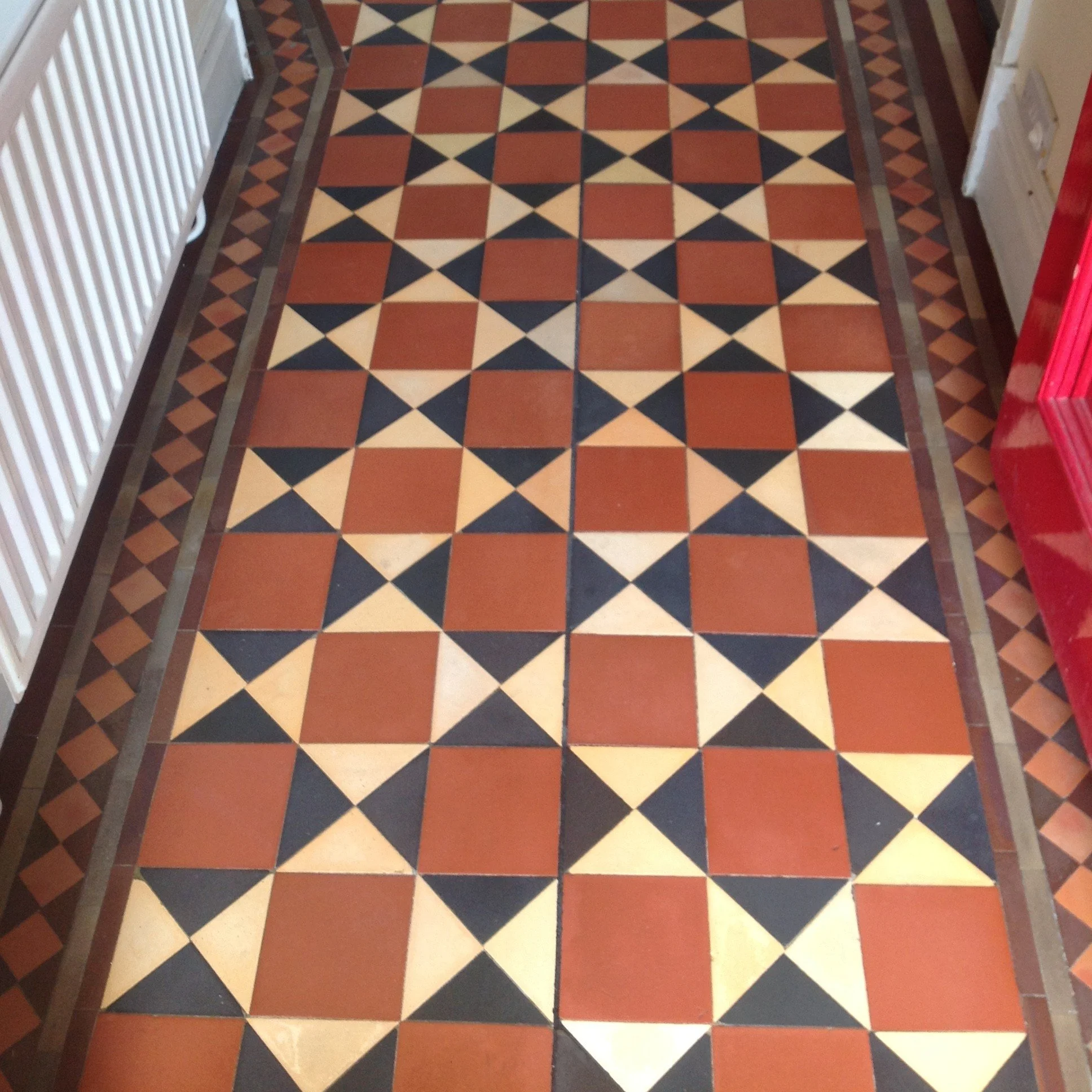 Patterned tile floor with geometric design in shades of red, black, beige, and brown, bordered by smaller diamond-shaped tiles.