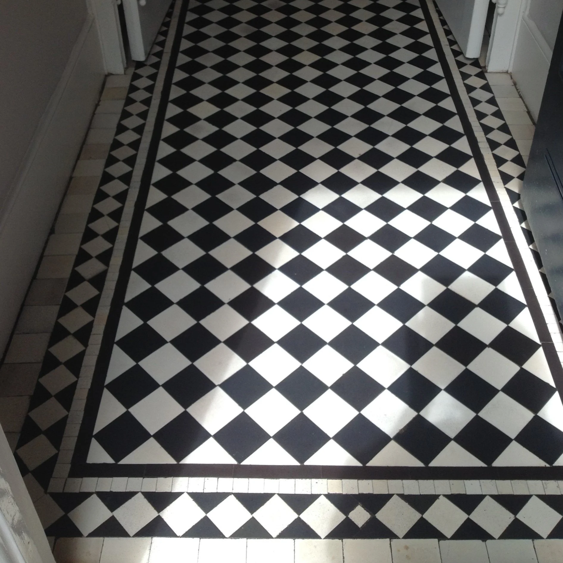 Black and white checkered tile floor with a decorative border in a hallway.