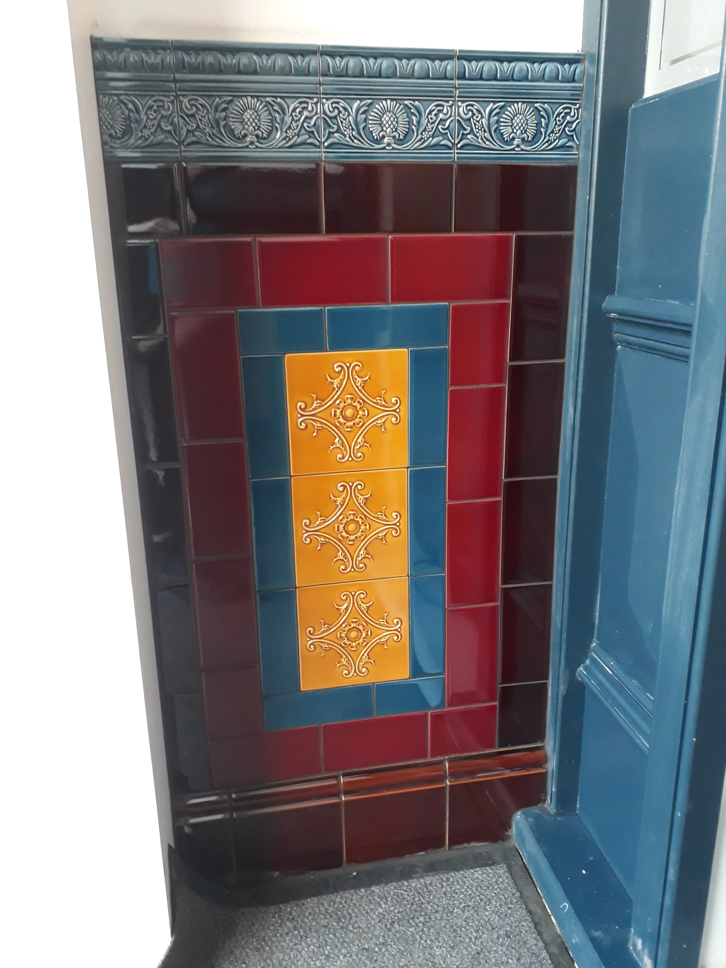 Decorative tiled wall with blue, red, and yellow tiles in a kitchen or bathroom setting.