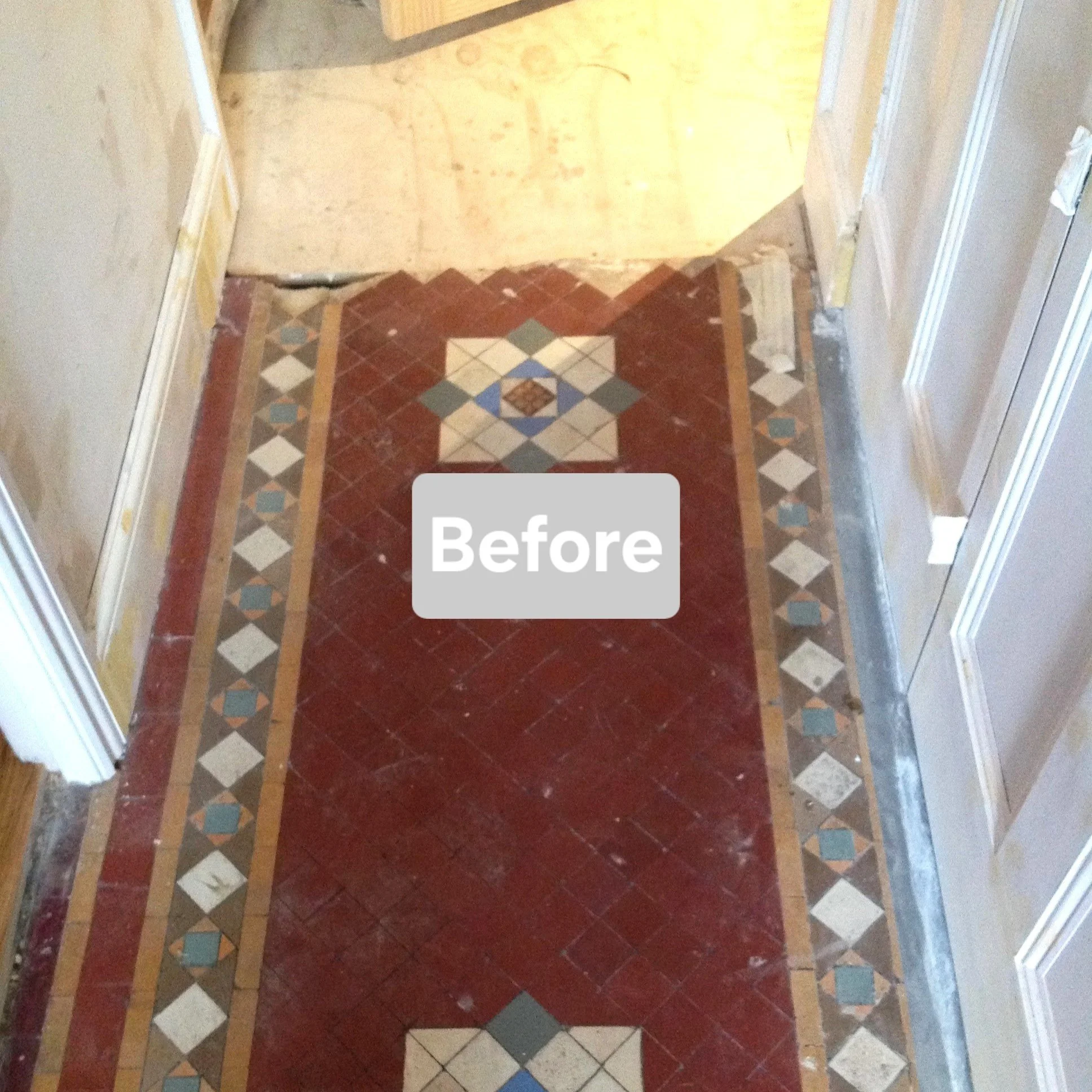 A hallway with a decorative tiled floor made of red, white, blue, and brown tiles, with some tiles showing signs of wear or paint splatters, and walls with white trim and beige paint, indicating it is in the process of renovation.