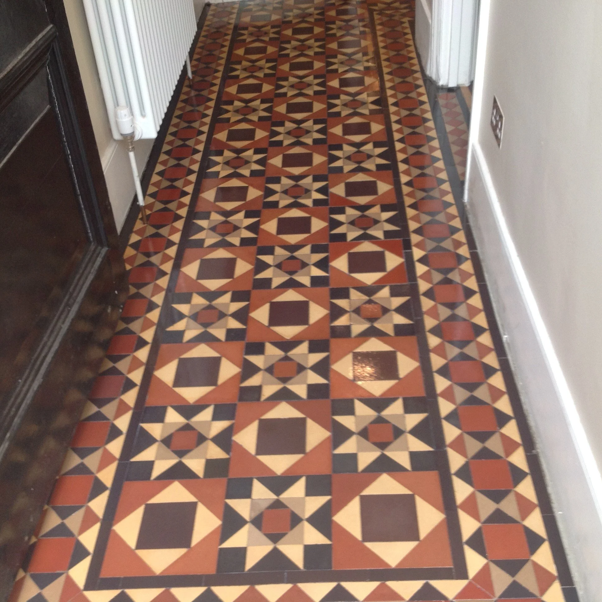 Decorative patterned tile floor in a hallway with geometric design in earth tones.