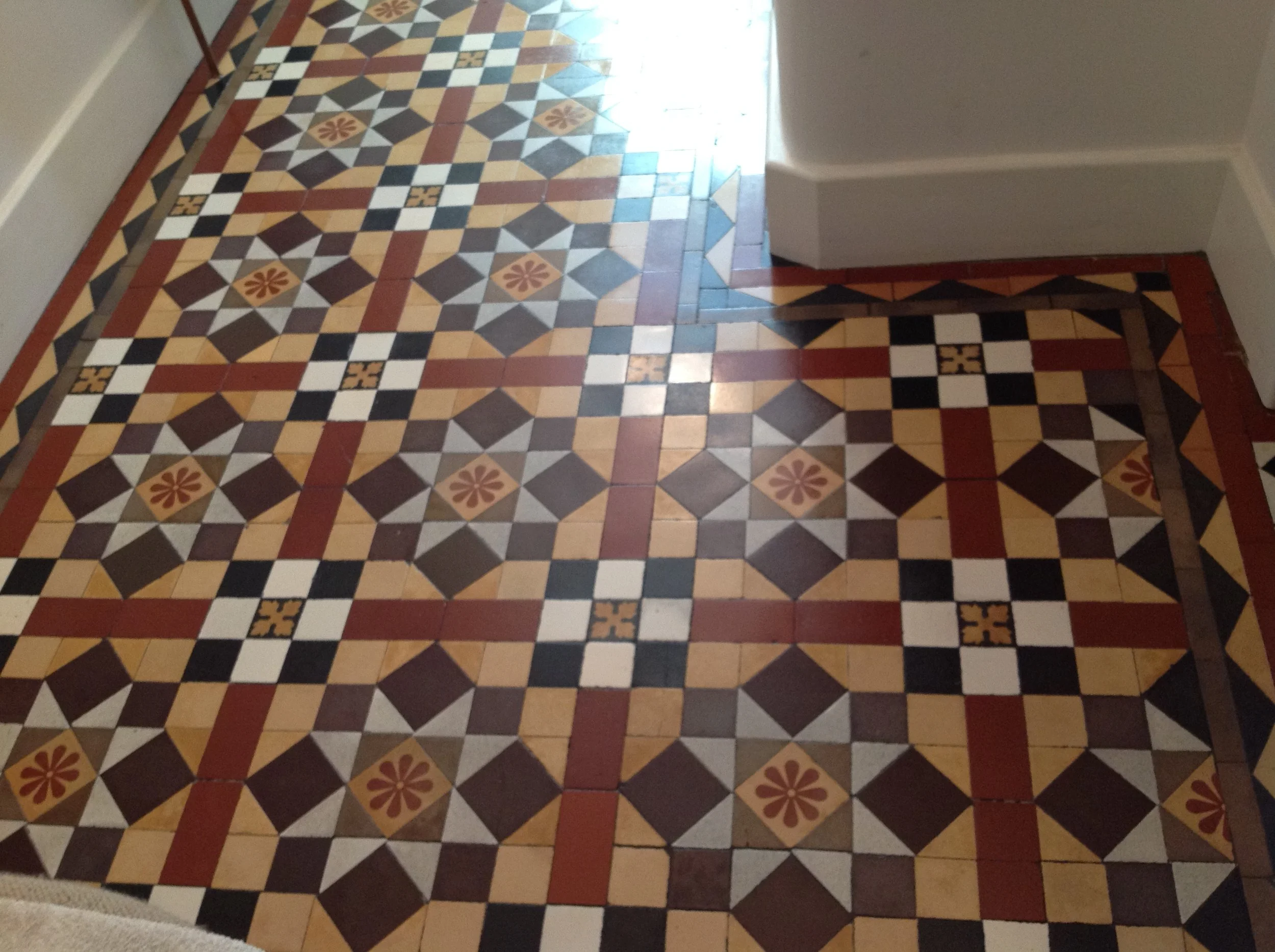 Decorative patterned tile floor in warm colors with geometric and floral designs, adjacent to a white wall and baseboard.