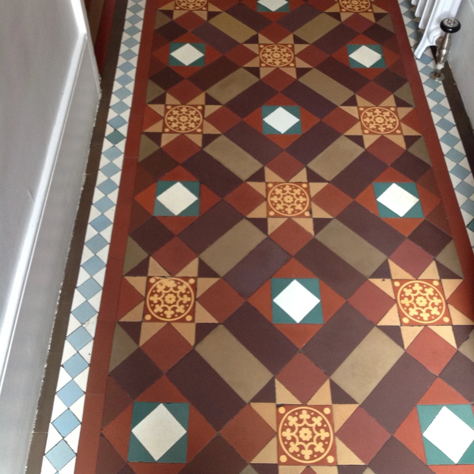 Decorative patterned tile floor with geometric and floral designs in various colors, bordered by a border of small blue and white diamond patterns.