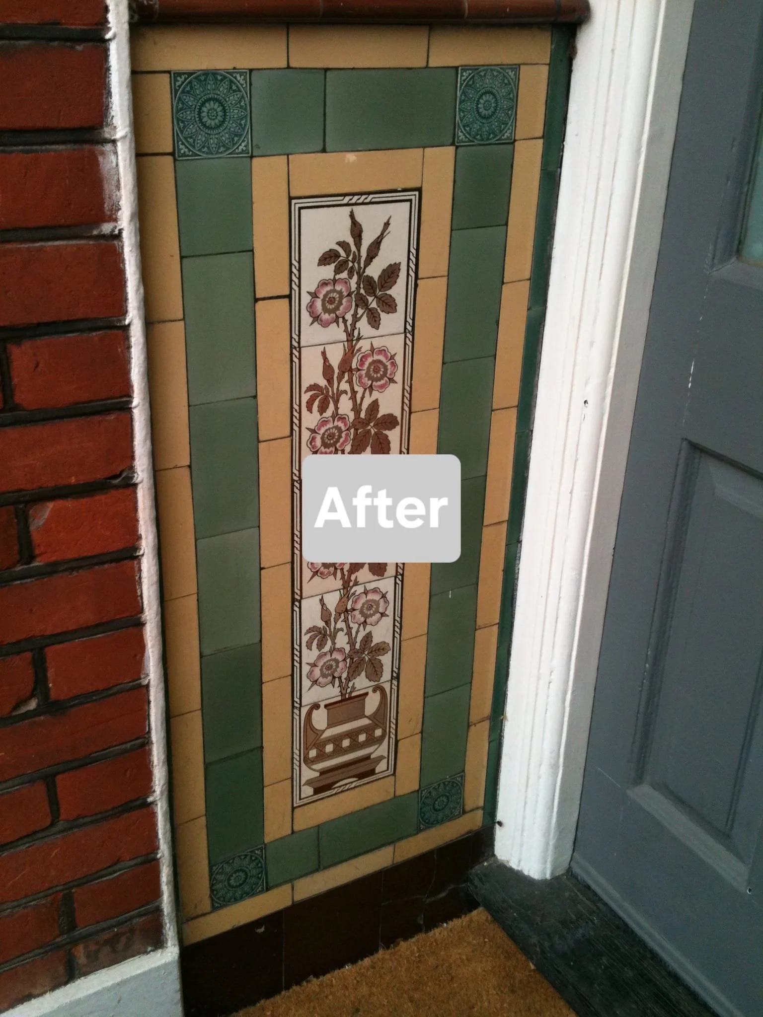 Decorative tiled panel with a floral design in front of a door and brick wall.
