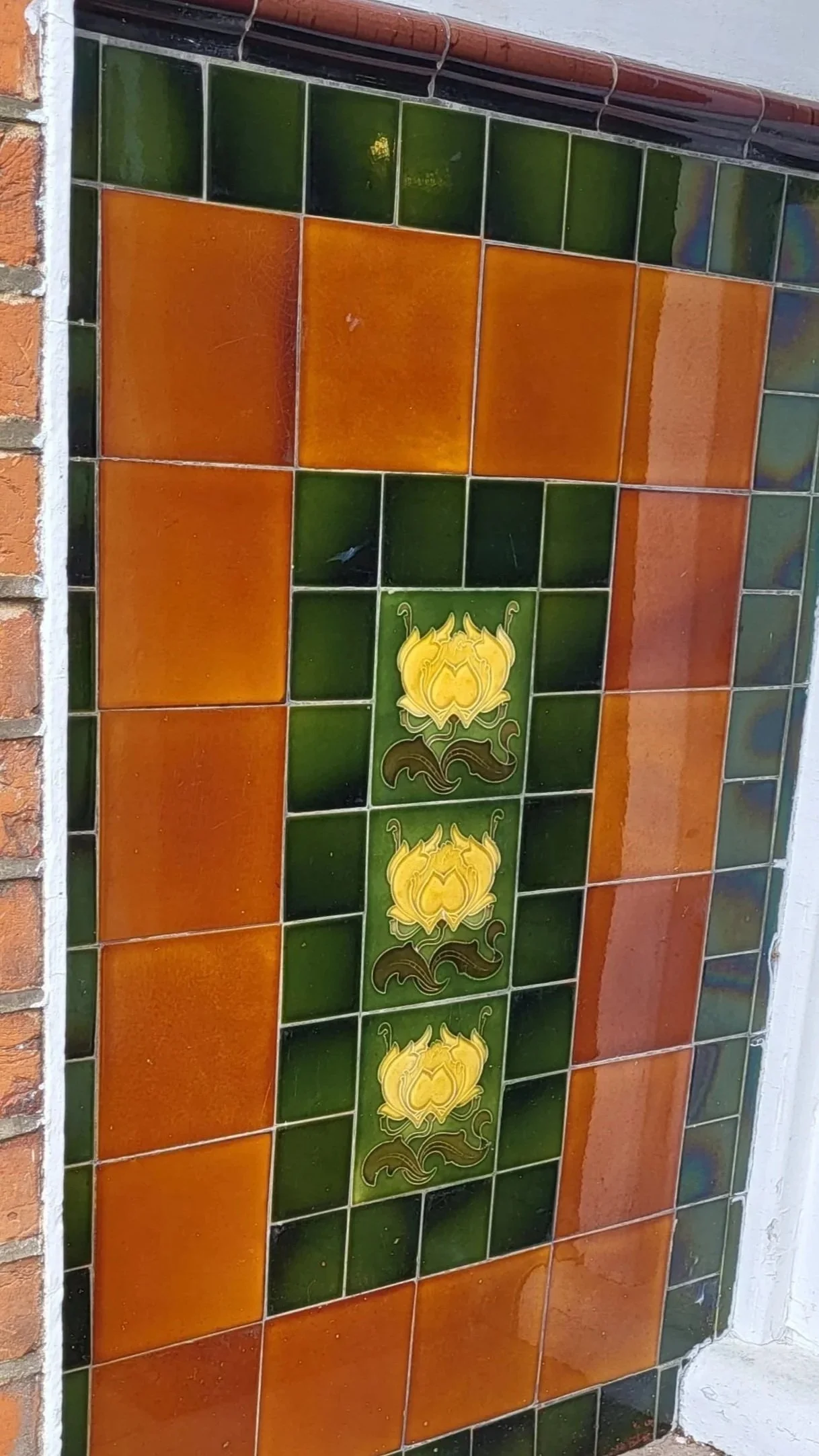 Decorative ceramic tile artwork featuring a yellow lotus flower with green and brown details, set against an orange, green, and brown tiled background.