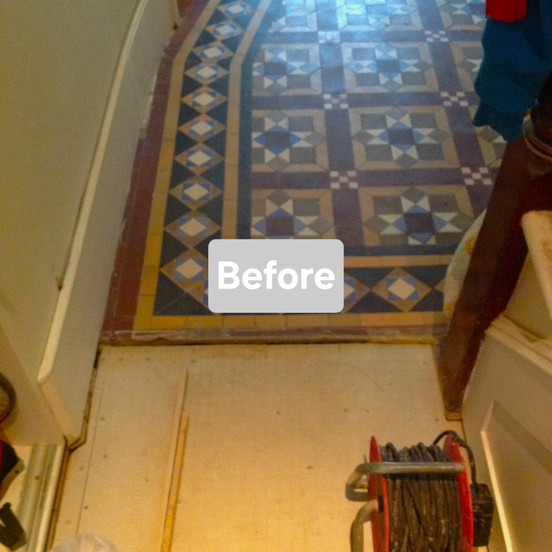Photo of a patterned area rug on a wooden floor, with a small step or threshold and a cart with cables in a room.