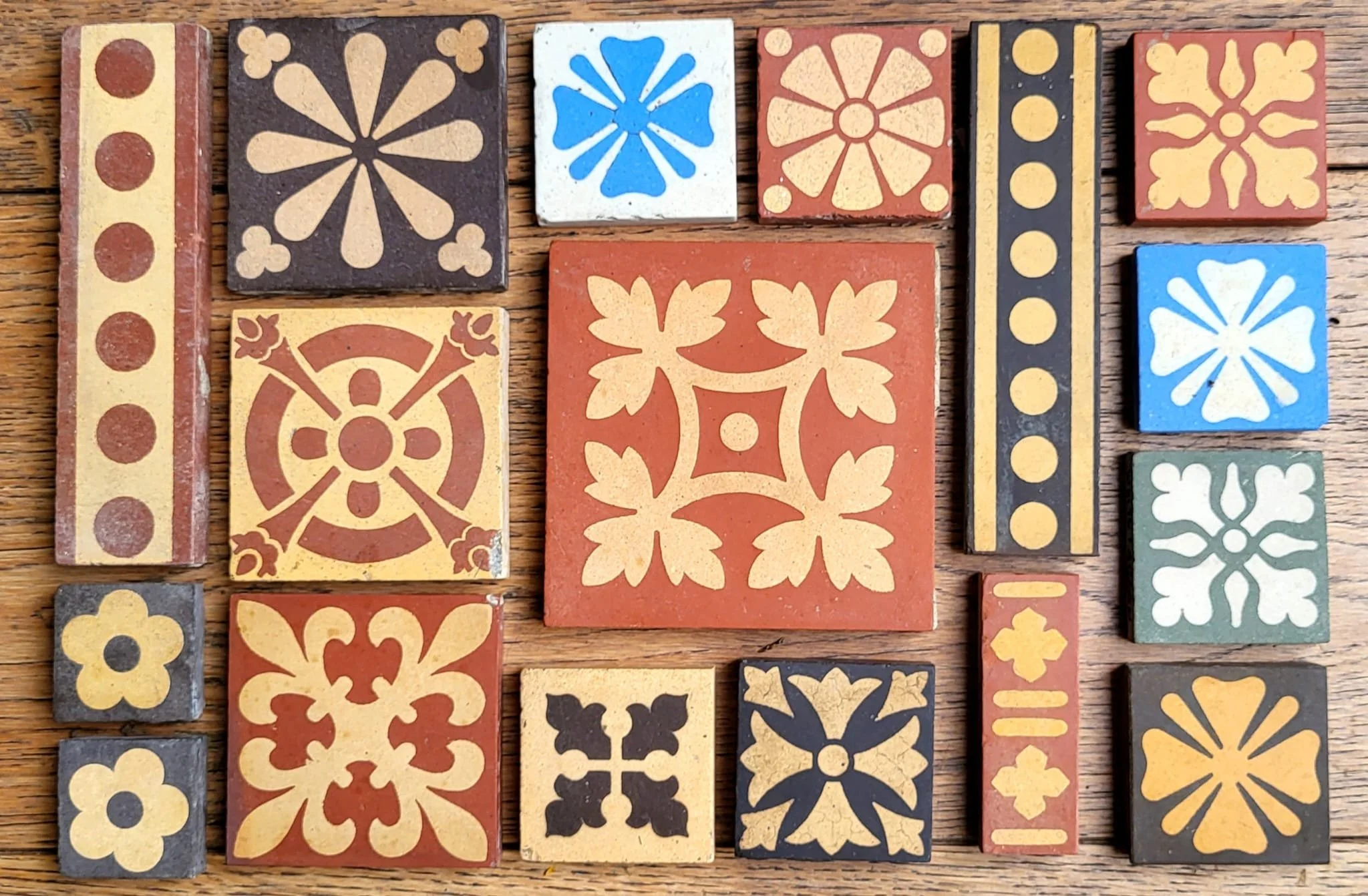Colorful vintage ceramic tiles with floral and geometric patterns in shades of yellow, black, white, red, and blue, arranged on a wooden surface.