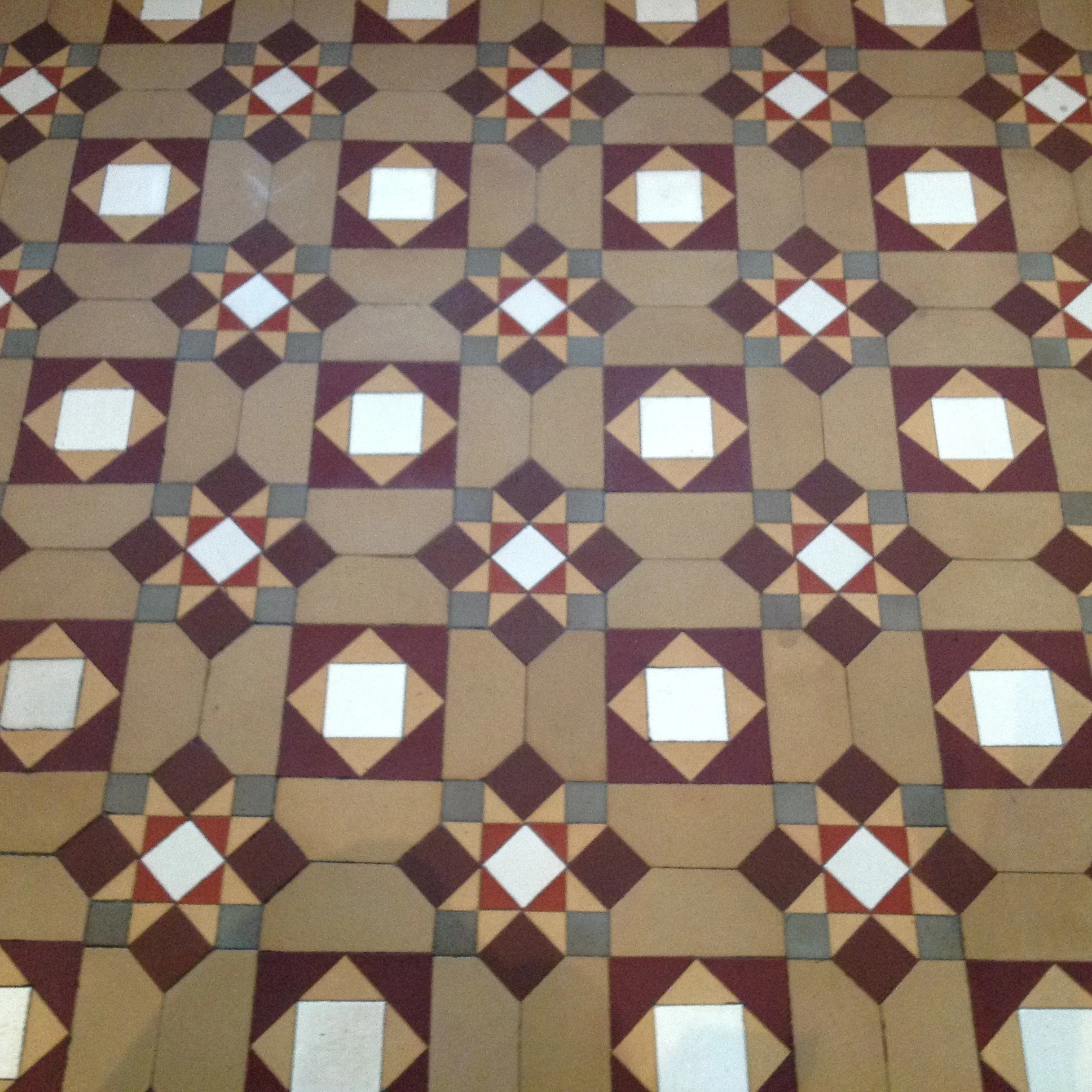 Patterned tile floor with geometric shapes in shades of beige, brown, white, and gray, arranged in a repeating symmetrical design.