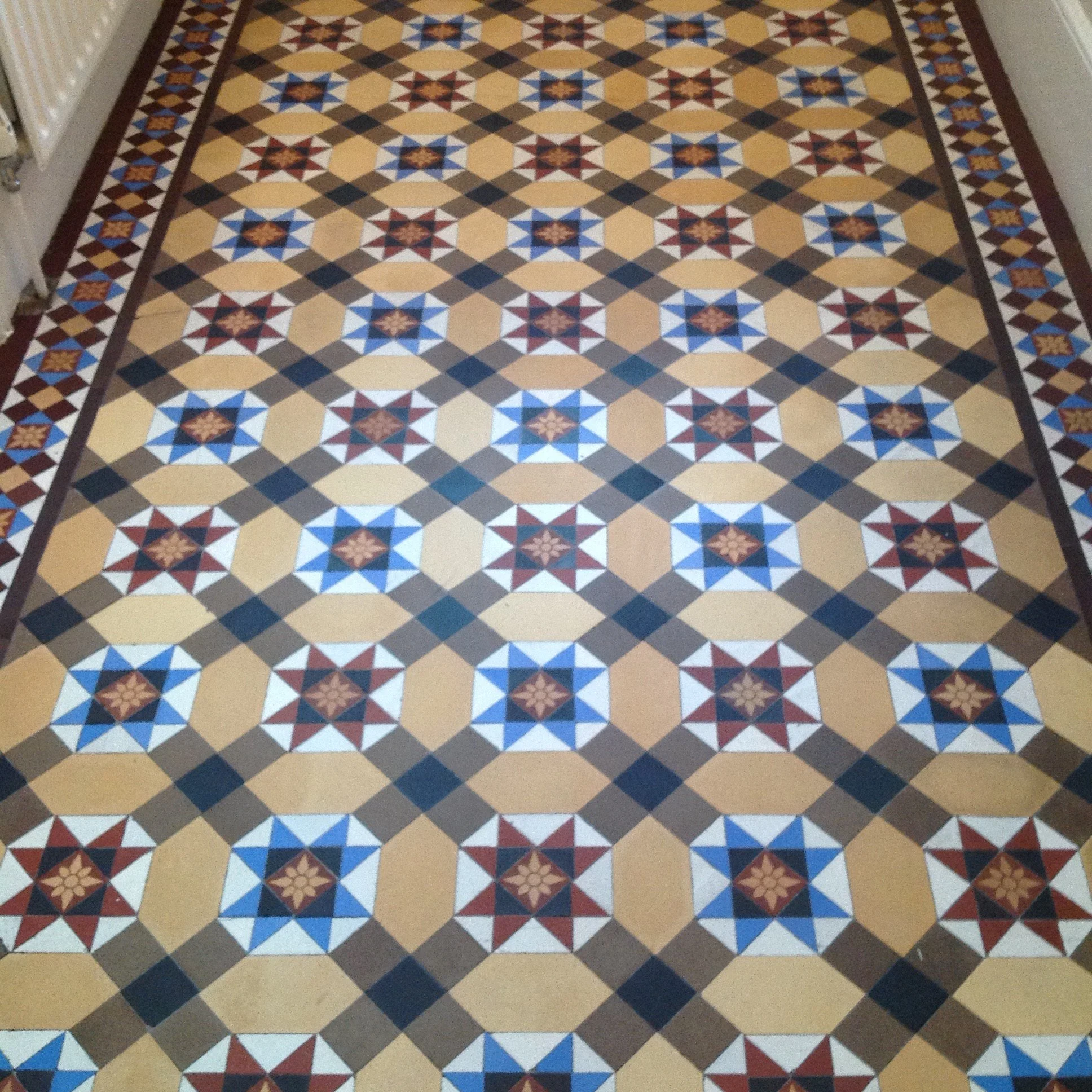 Decorative floor with a geometric tile pattern featuring stars and octagons in shades of red, blue, beige, and black, with a bordered edge.