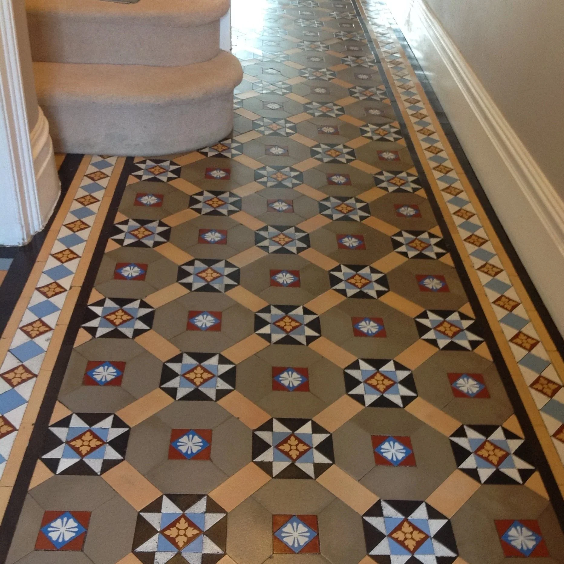 Decorative patterned tile floor with a border, featuring various geometric shapes and colors, including beige, black, blue, red, and yellow, in an indoor setting.