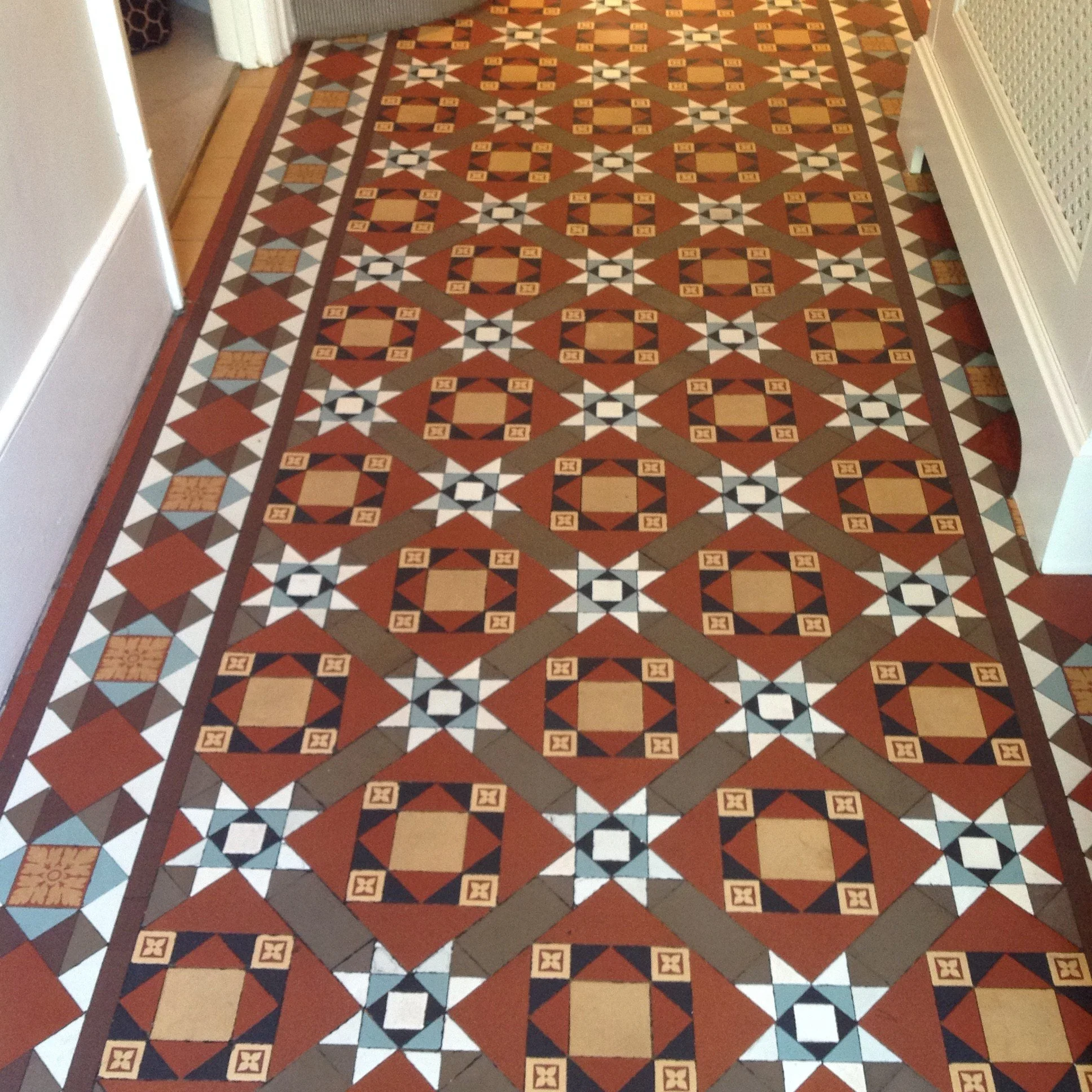 Decorative tiled floor with geometric patterns in red, black, white, beige, and gray colors, styled in a symmetrical repeating design along the hallway.