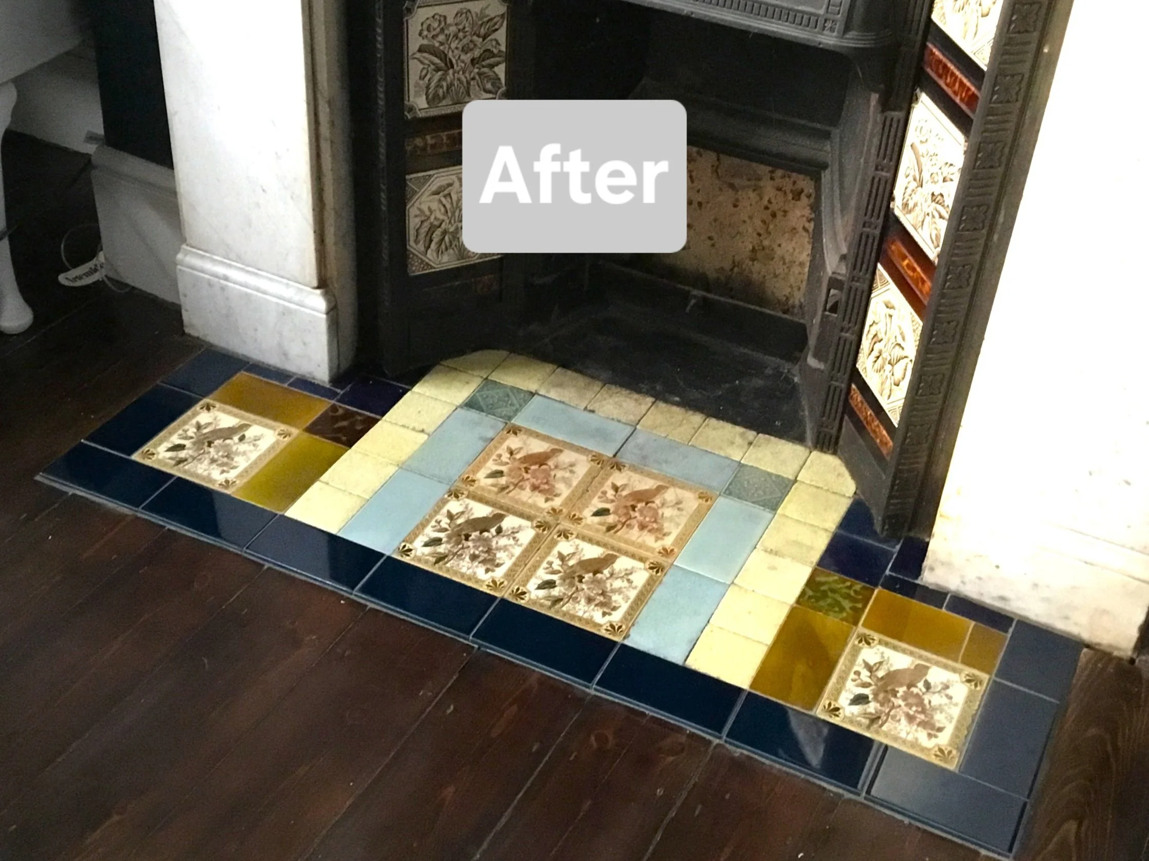 Renovated fireplace with colorful decorative tiles around the base, featuring floral patterns and a black wood structure inside the fireplace.