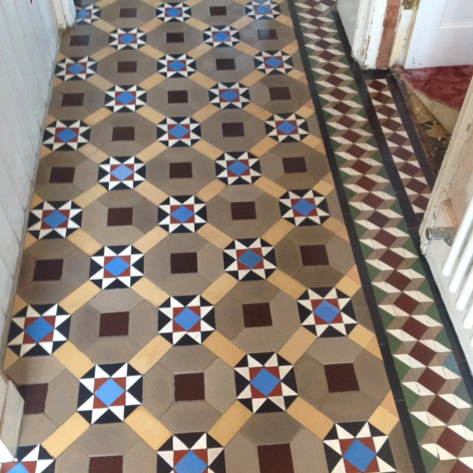 Decorative patterned floor tiles with geometric designs in shades of brown, black, beige, blue, white, and red, arranged in a repeating pattern along the hallway.