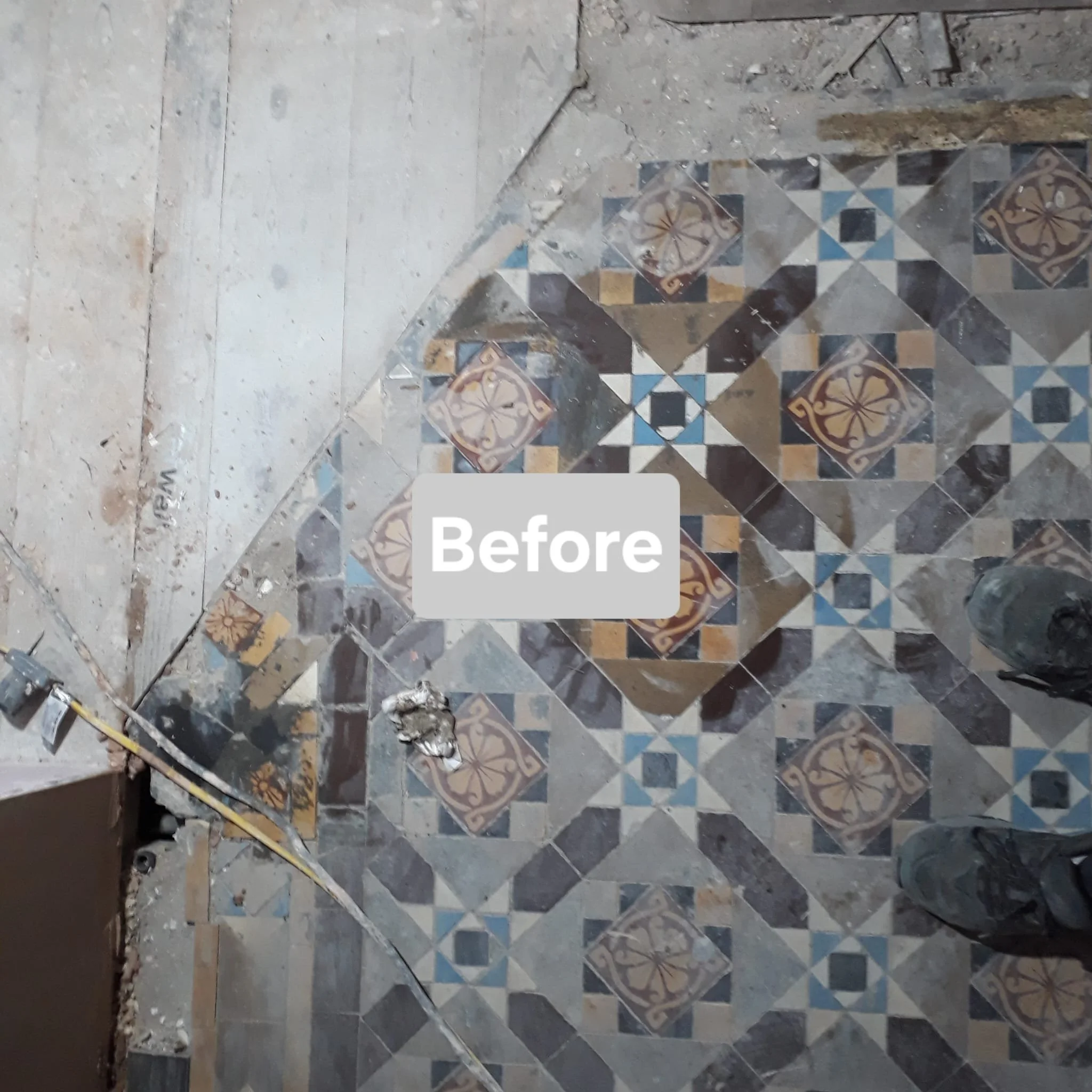 Old decorative floor with intricate multicolored tile pattern, partially covered with construction dust and debris, in a space under renovation.