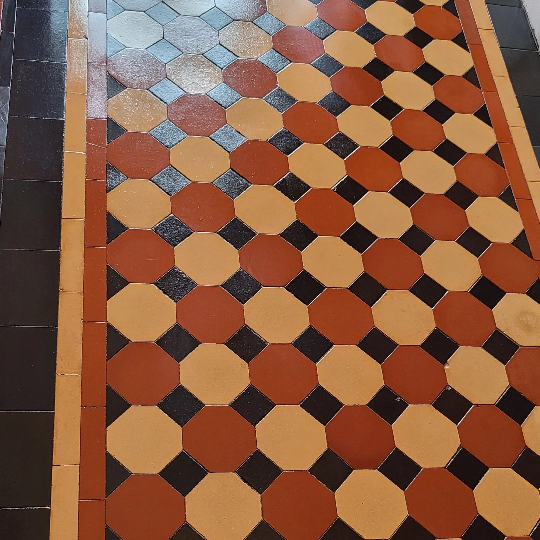 Close-up of a patterned floor with terracotta, black, and beige hexagonal tiles and border tiles.