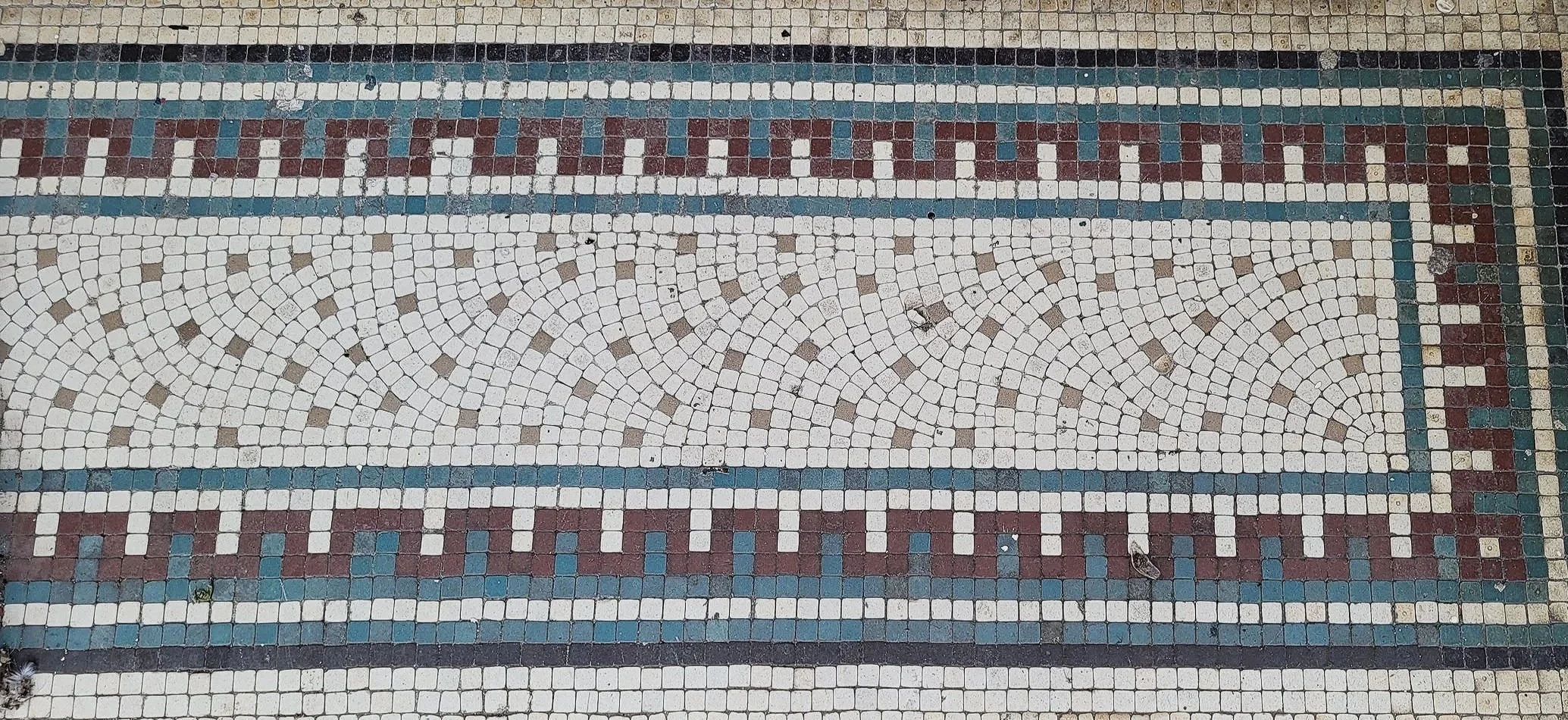 Close-up of decorative mosaic tile floor with geometric patterns in white, brown, blue, and green colors.