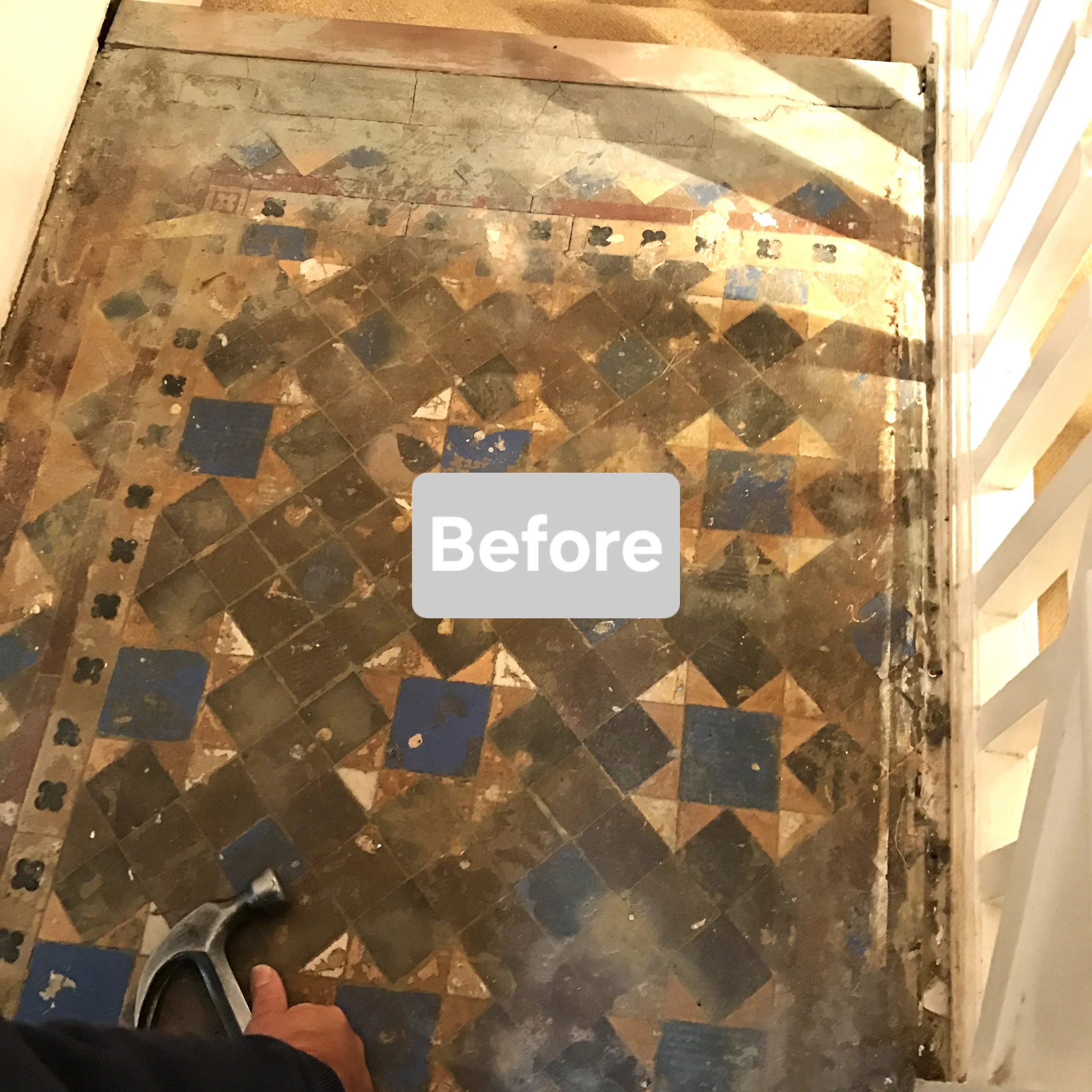 Old, worn mosaic tile floor with a decorative pattern in shades of brown, black, and blue, partially cleaned with a person using a scrub brush in the lower left corner.