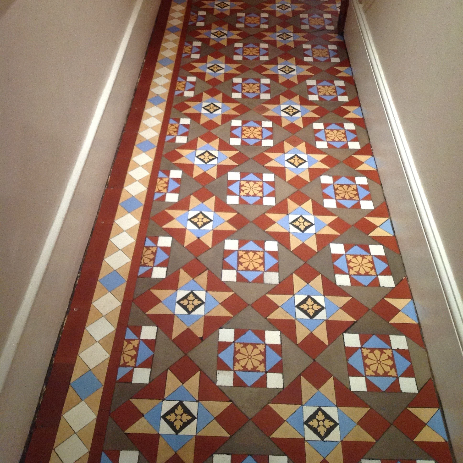 Colorful geometric tile floor in a hallway with cream-colored walls and baseboards.