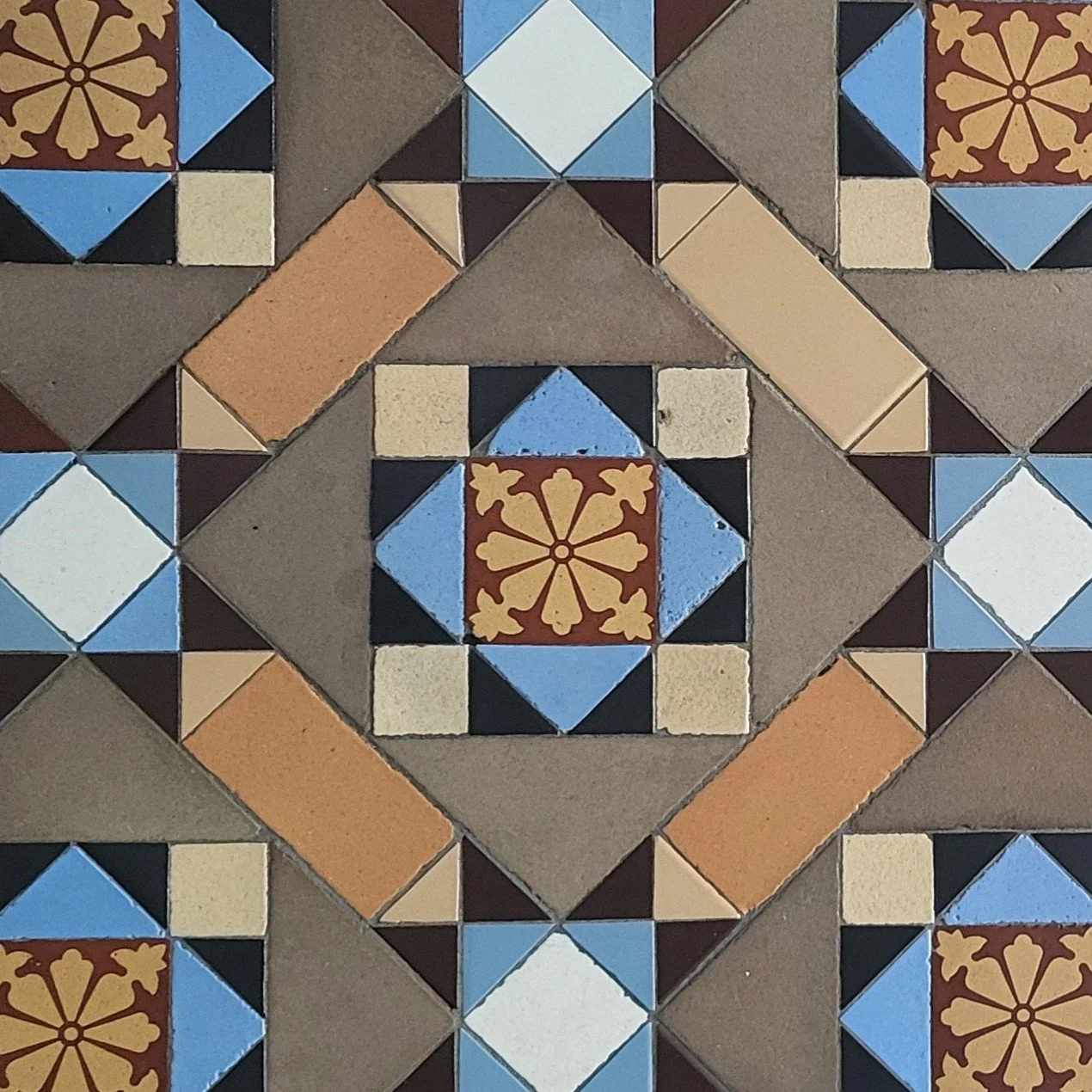 Patterned ceramic tiles in a geometric design with colors including brown, black, beige, blue, and white, forming a symmetrical pattern with floral motifs.