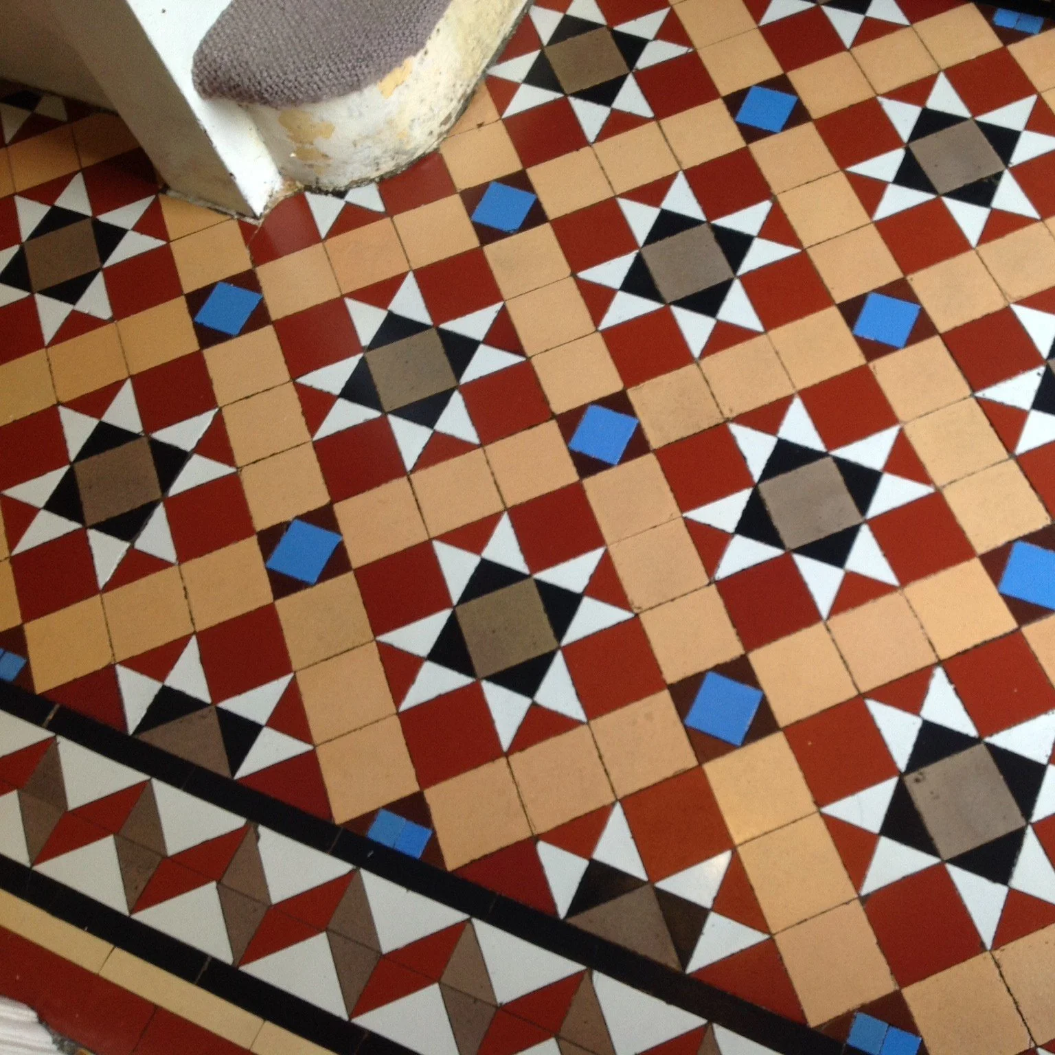 Colorful geometric mosaic tile floor with patterns of black, white, red, beige, and blue tiles in a repeating design.