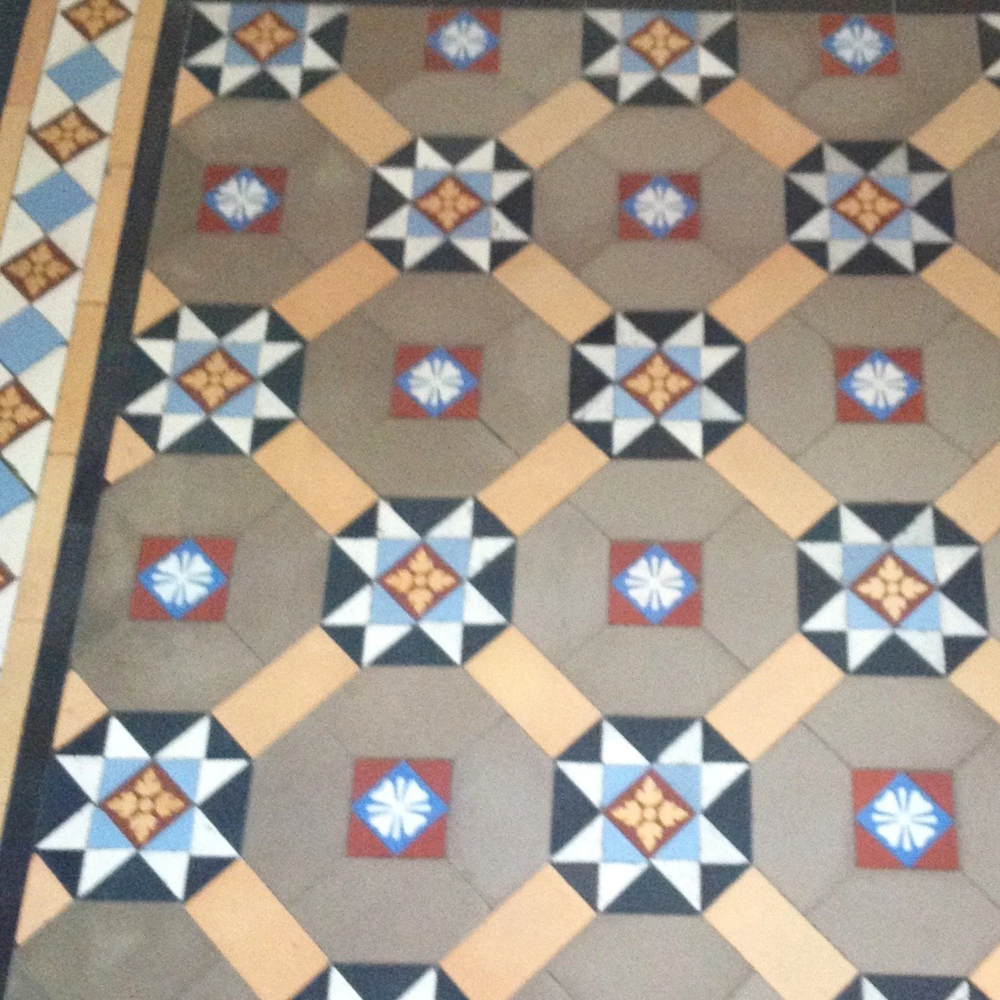 Patterned tile floor with four hexagons in coffee tiles forming a circular shape and a star motif all joined with a yellow frame. Classic Victorian design 