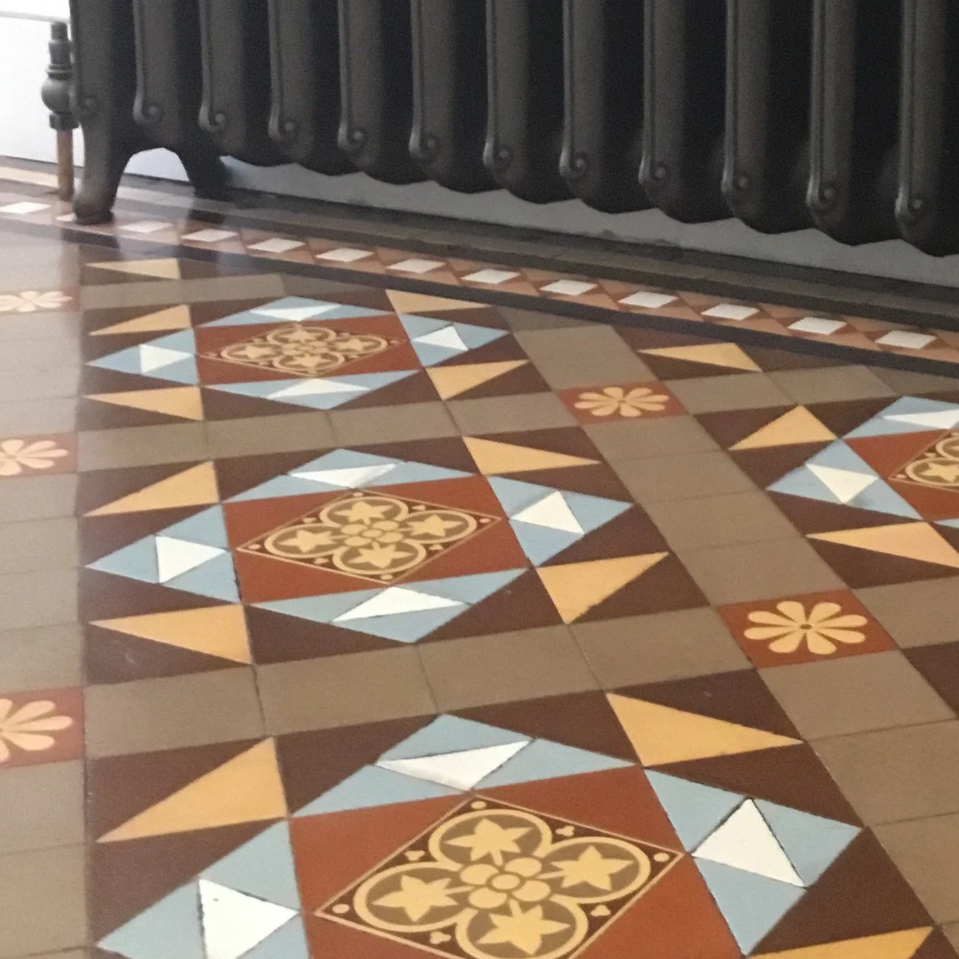 Decorative tiled floor with geometric patterns and floral motifs, positioned beneath a black radiator.