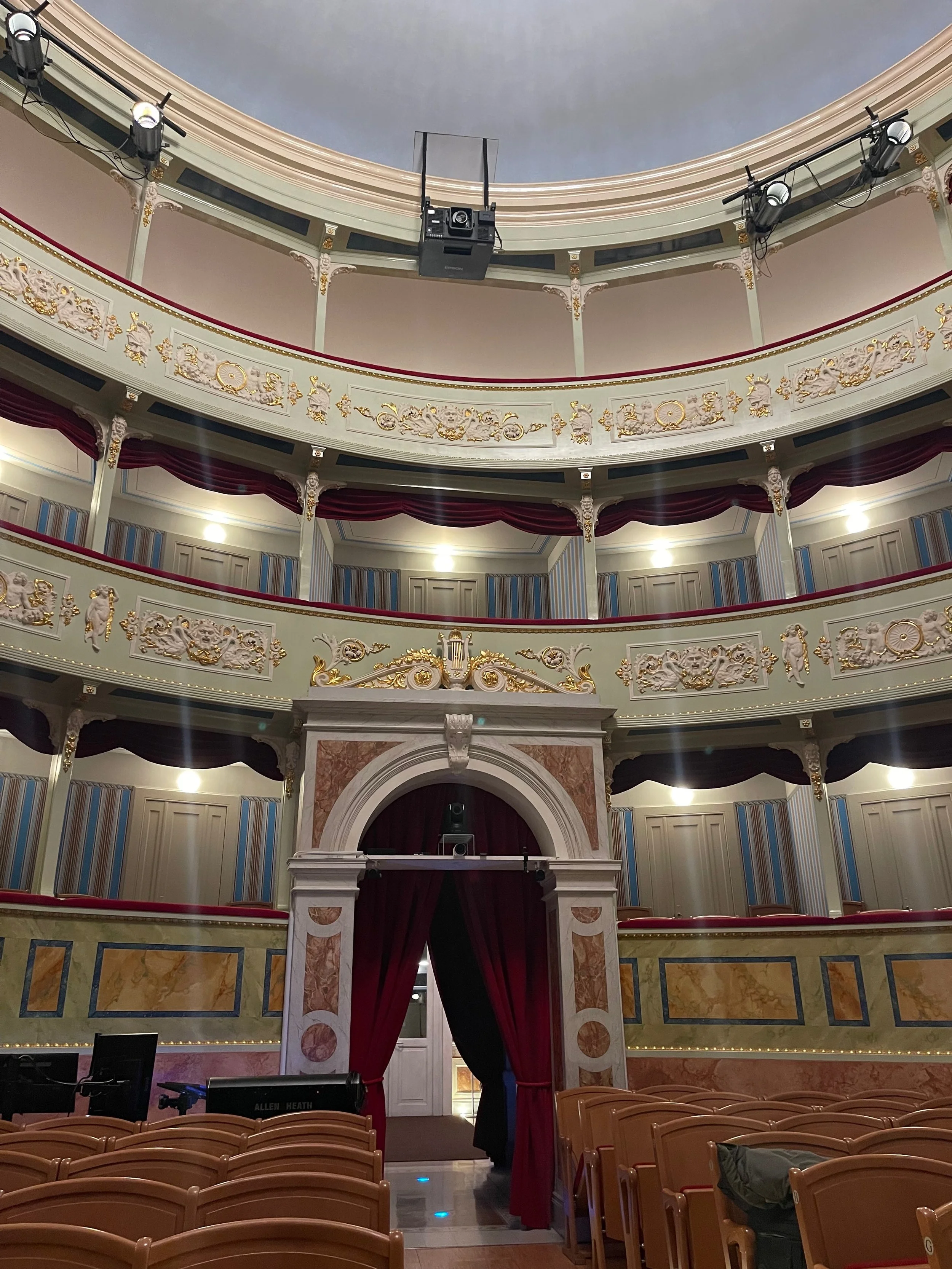 Intérieur d'un théâtre avec des balcons ornés de décoration dorée, rideaux rouges et scène au fond avec un rideau fermé.