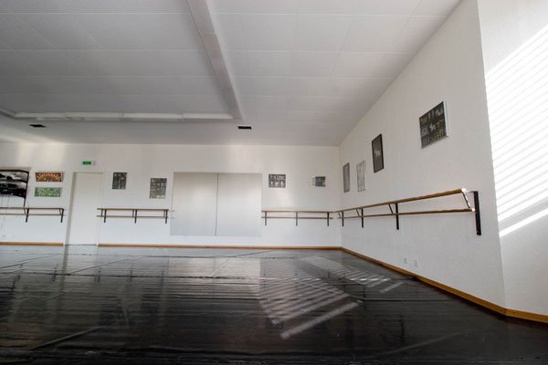 Une salle de danse vide, des bars de ballet fixés au mur blanc, et des œuvres d'art encadrées accrochées sur le mur droit.