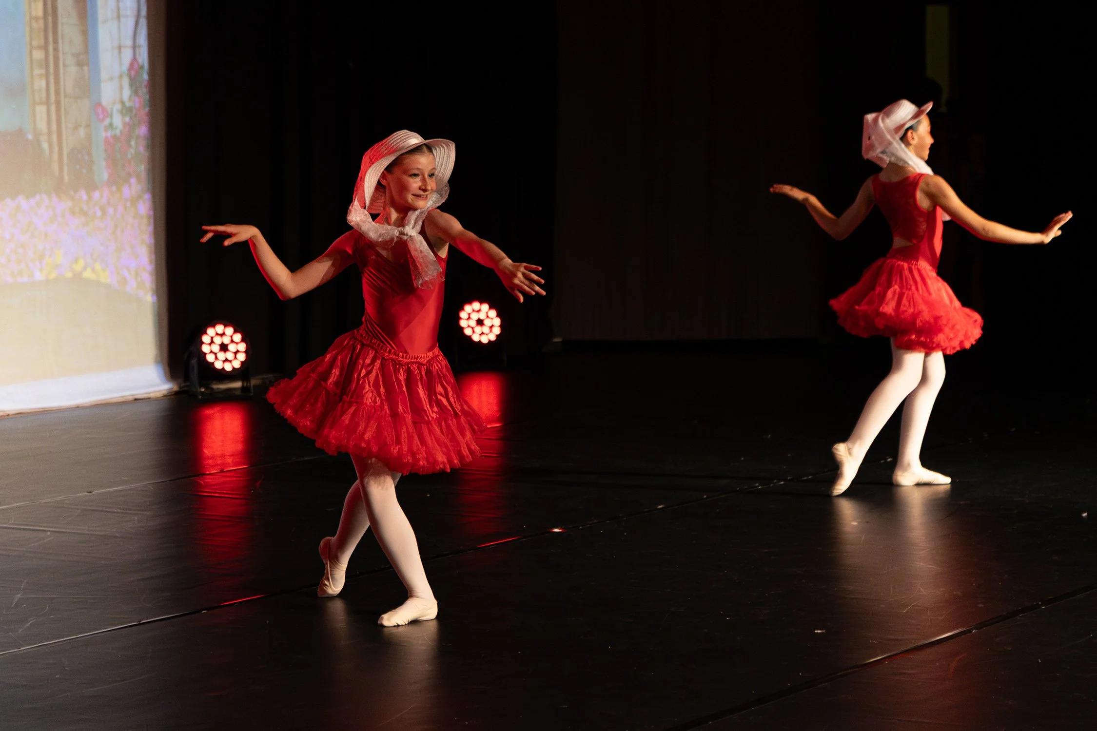 Deux jeunes filles en costumes de danse rouges, portant des chapeaux de paille, dans un spectacle de danse sur scène.