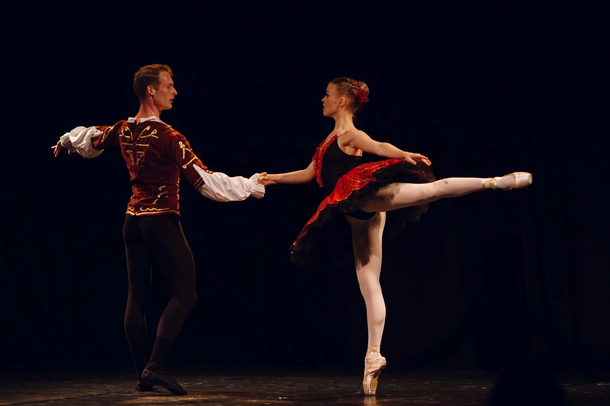 Deux danseurs classiques en costume lors d'une représentation, la femme en position de pirouette sur la pointe et l'homme tenant sa main.
