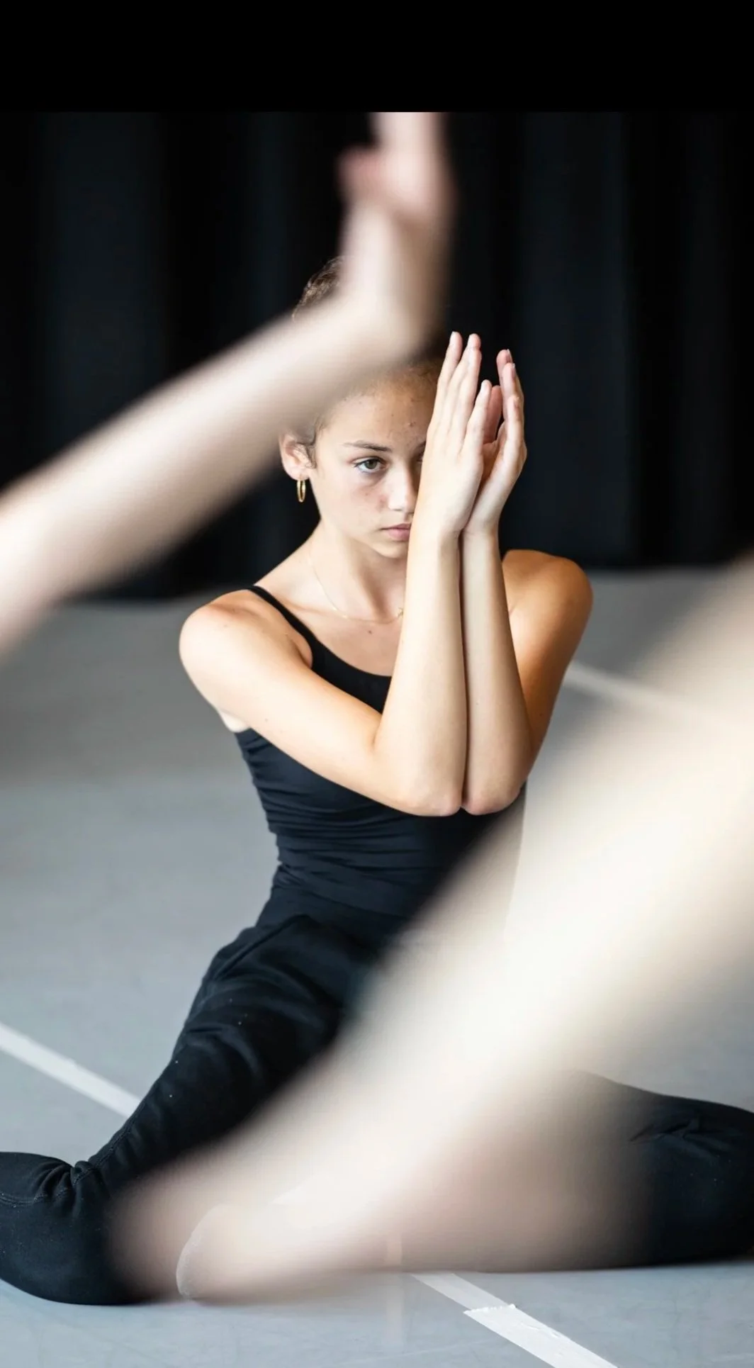 Une jeune ballerine en position d'étirement sur un sol de studio, stretching geneva dance center